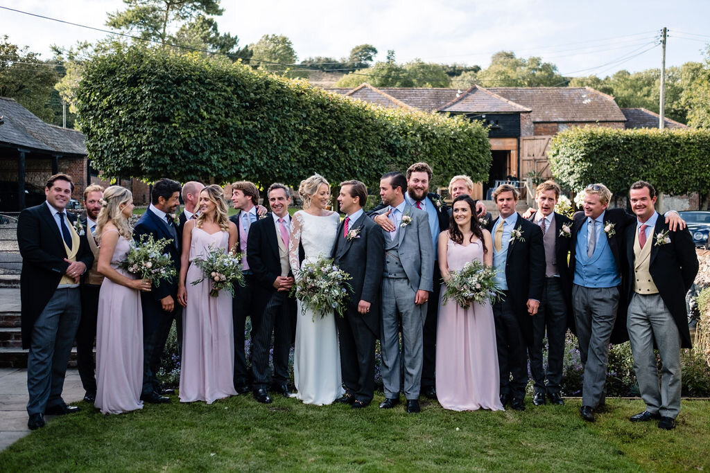 large wedding party of ushers and bridesmaids in pink standing in a row