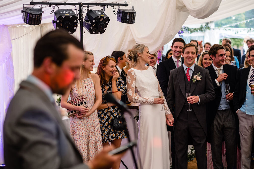 bride and groom in marquee laughing and listening to speeches