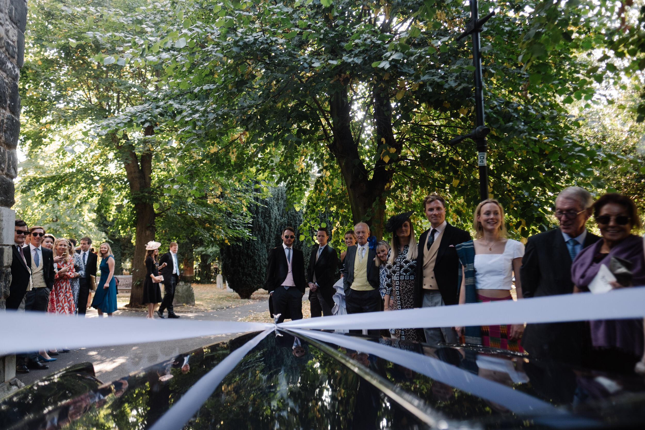 view through wedding car window of ribbon and guests waving off couple