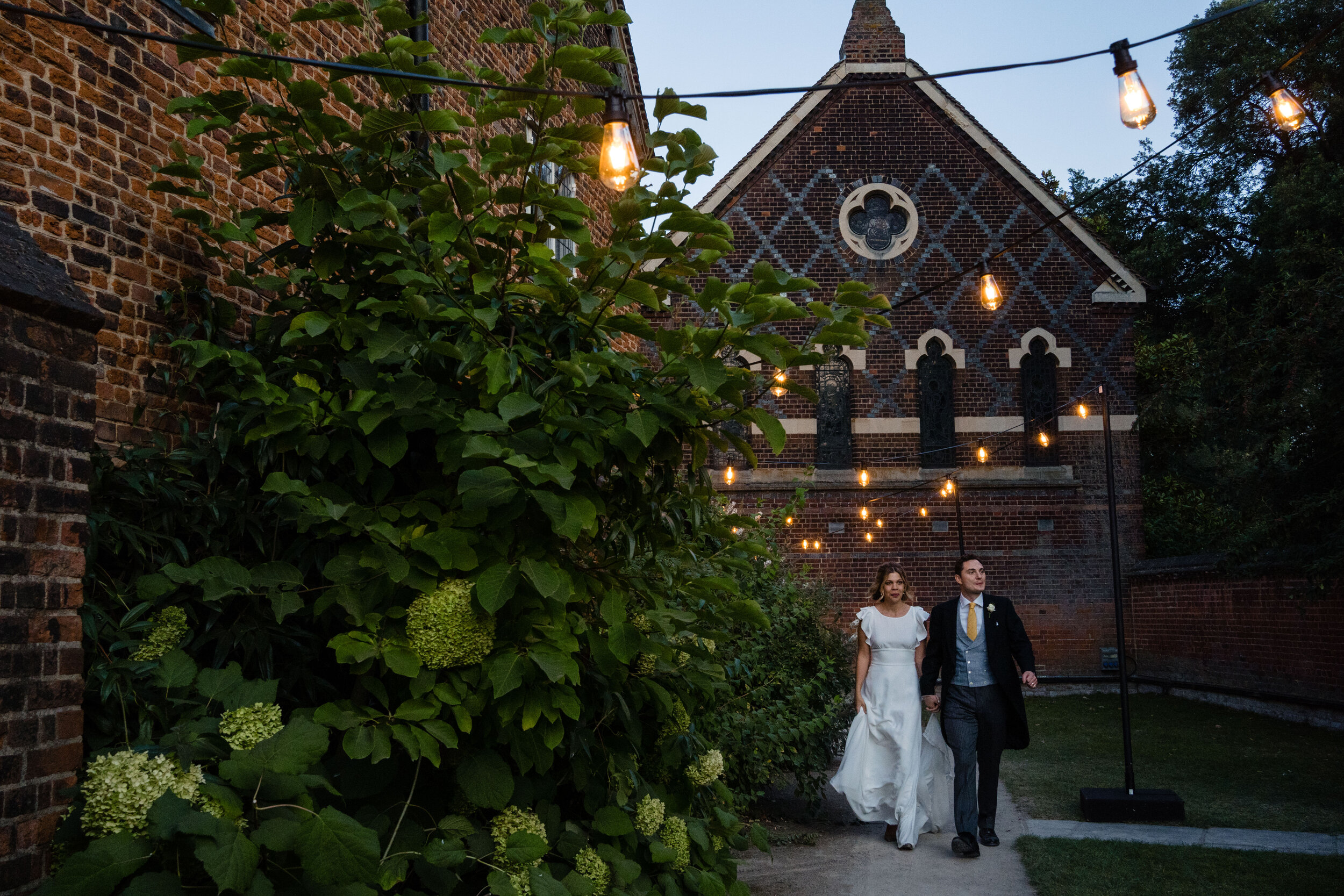 couple walking through garden with fair lights at Fulham palace