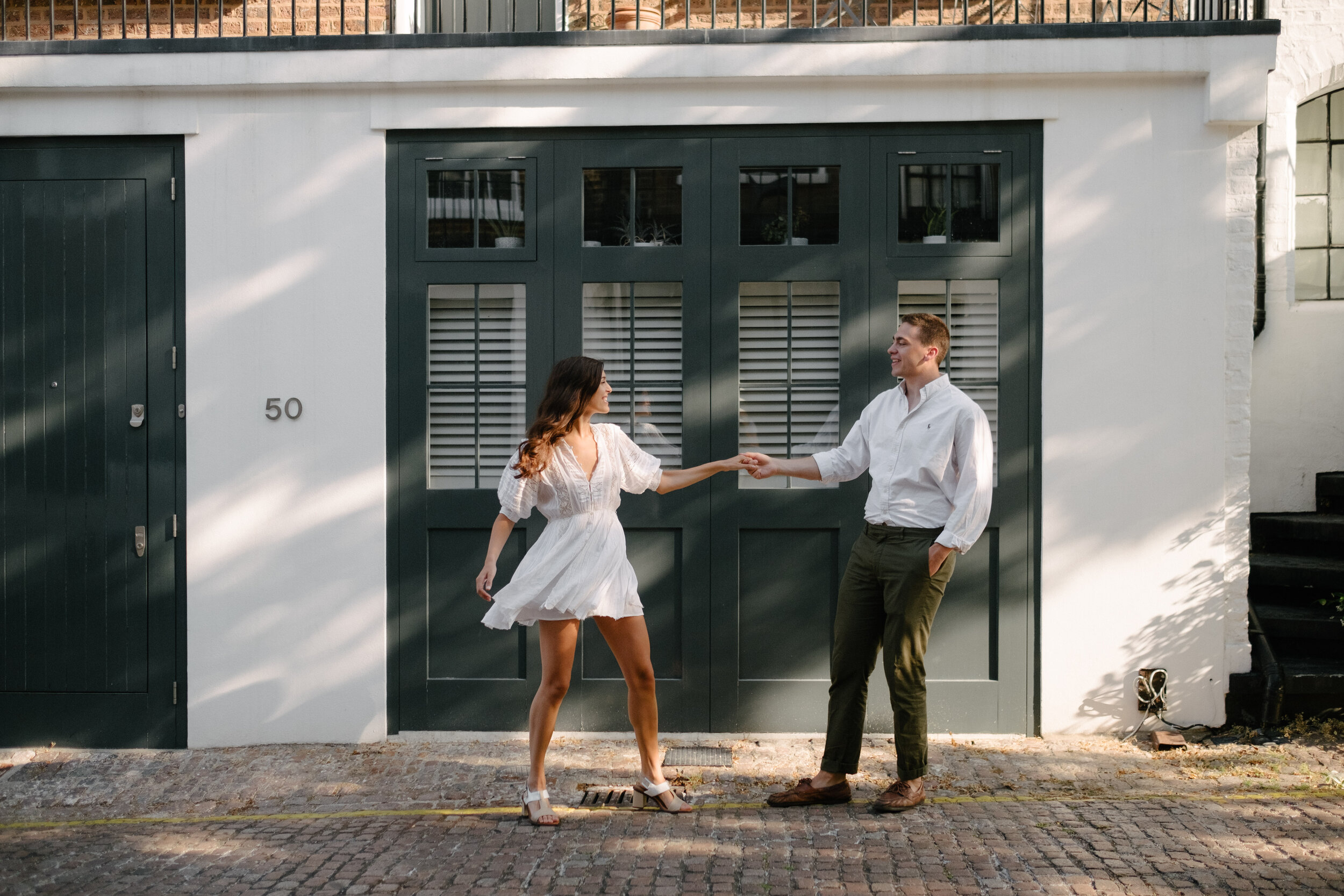 couple dancing in front of green doors in London mews she is wearing short white dress 