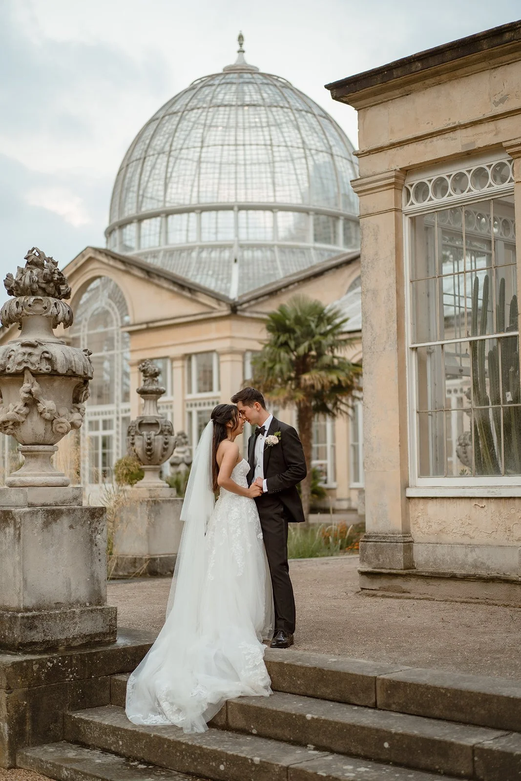 Bride and groom embracing on the steps outside the Glasshouse at Kew Gardens during their London wedding, photographed by London wedding photographer Helen Abraham.