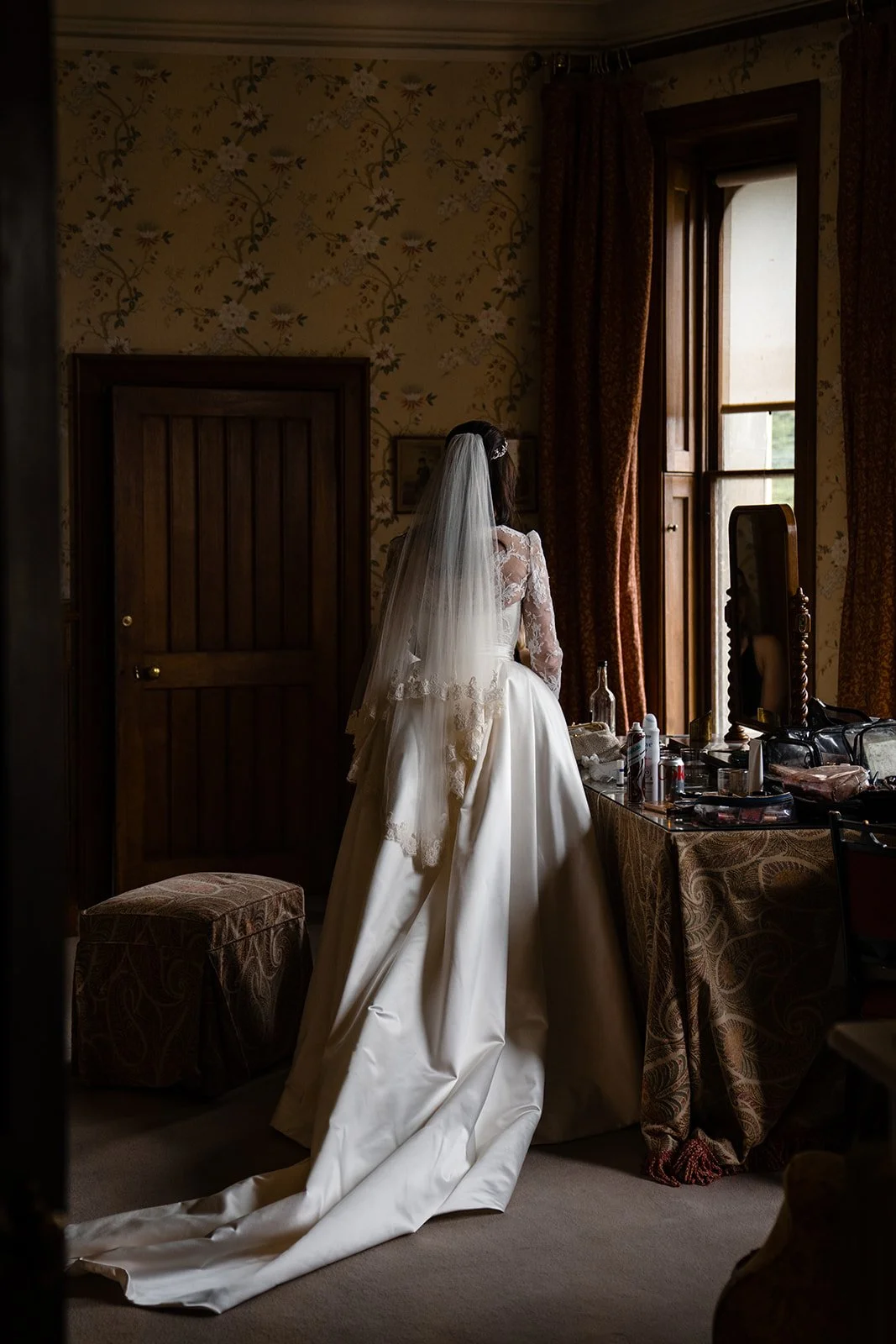 Bride standing by a window in her wedding dress while getting ready in a historic country house