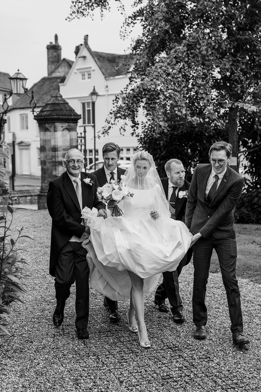 Bride walking with her groomsmen during a London wedding, photographed by London wedding photographer Helen Abraham. Natural documentary moment in black and white.