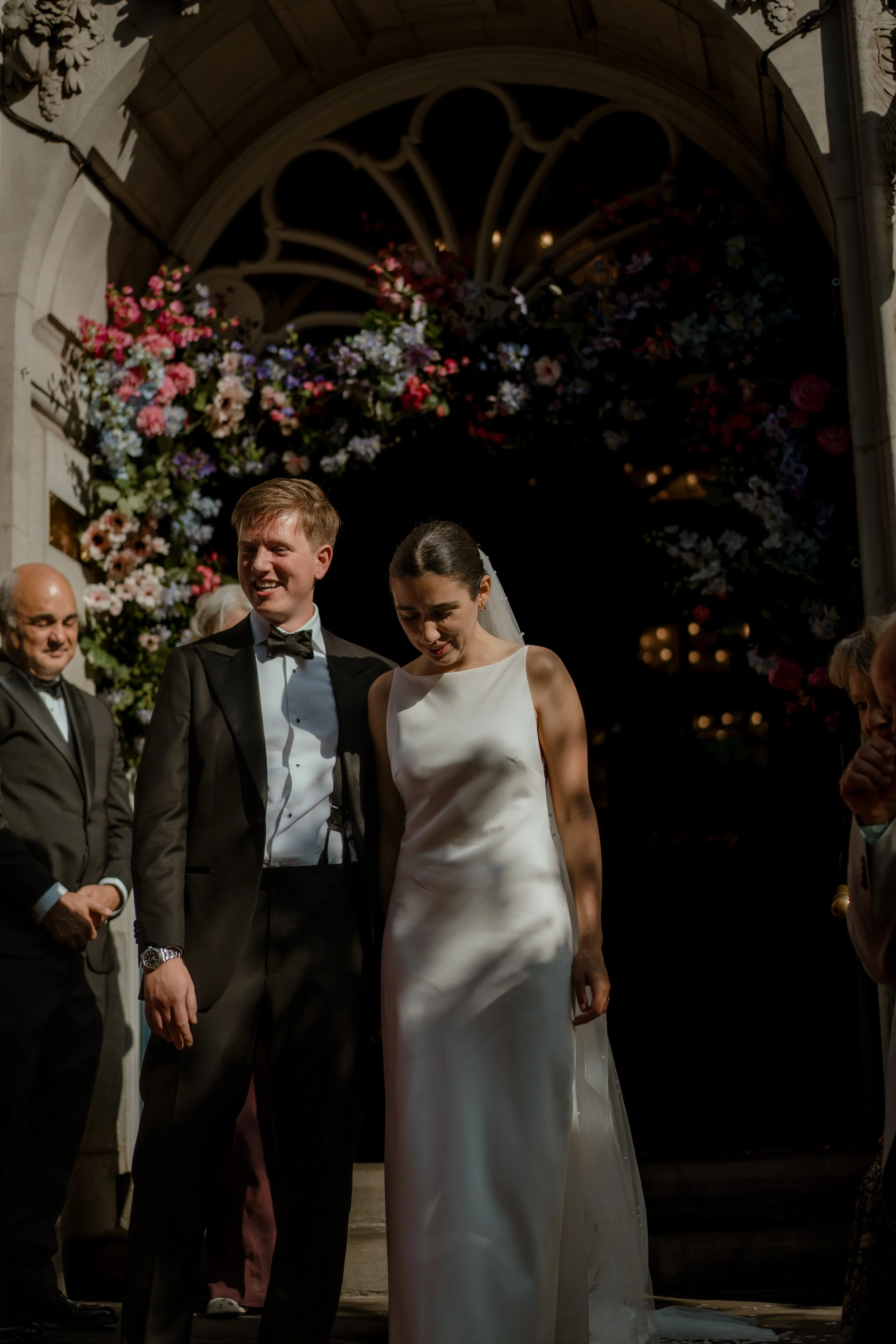 Bride and groom leaving the main entrance of Chelsea Old Town Hall surrounded by guests and with a flower canopy.