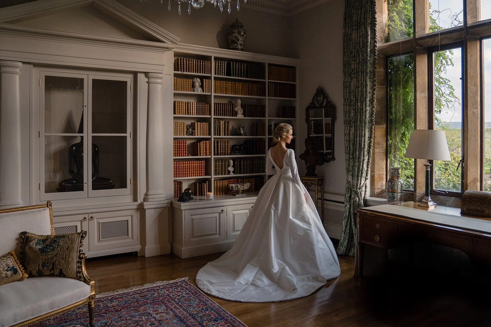Bride standing near a large window with soft natural light creating a timeless portrait.