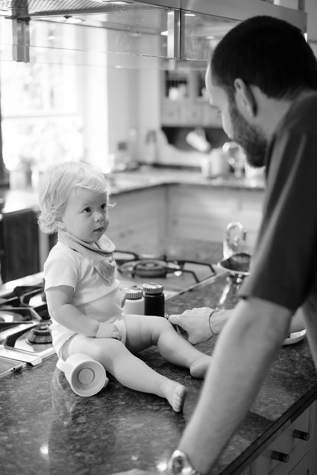 Small child sitting on a kitchen counter talking with a parent during quiet morning preparations
