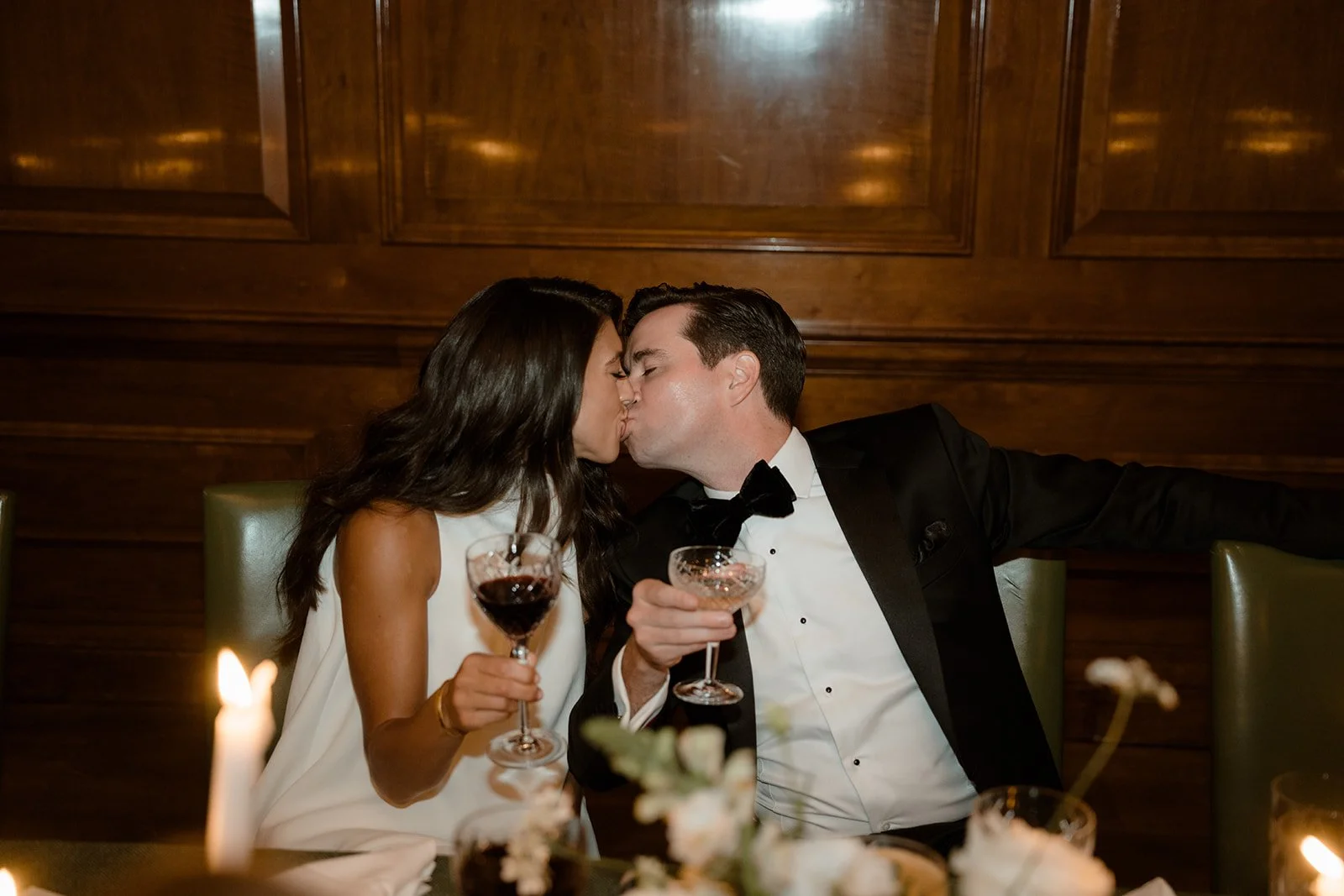 Bride and groom kissing while holding champagne glasses at their wedding reception.