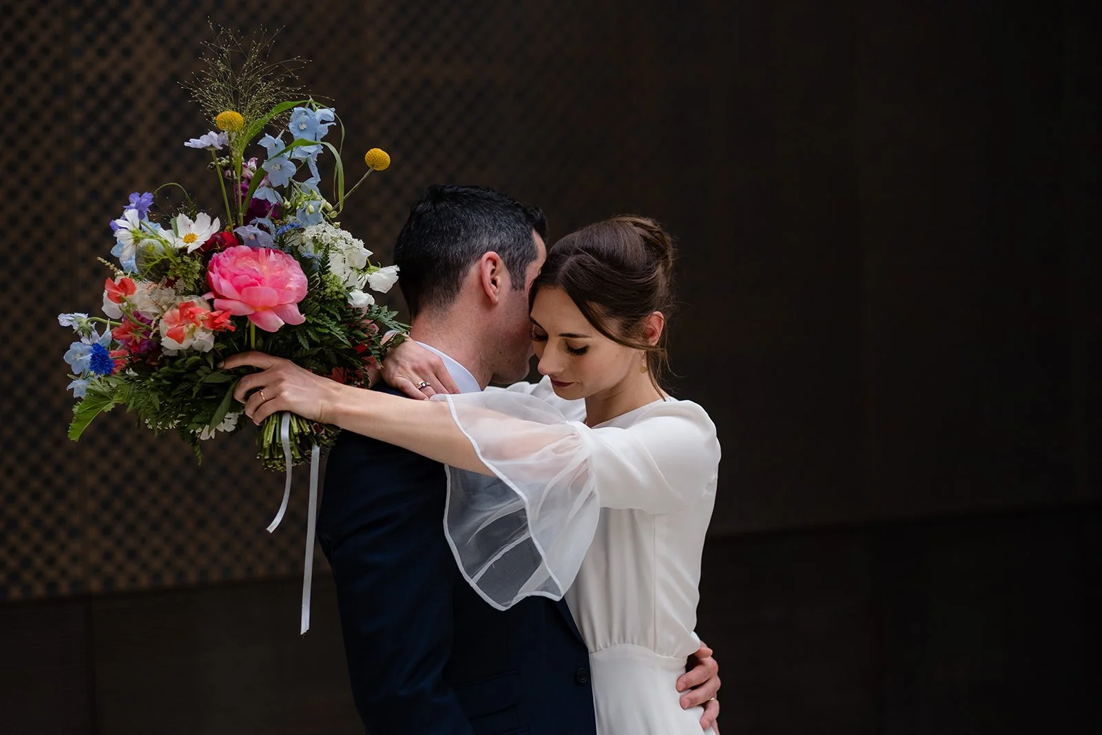 Bride embracing the groom while holding a large bouquet of bridal flowers at Hackney Town Hall after a London wedding