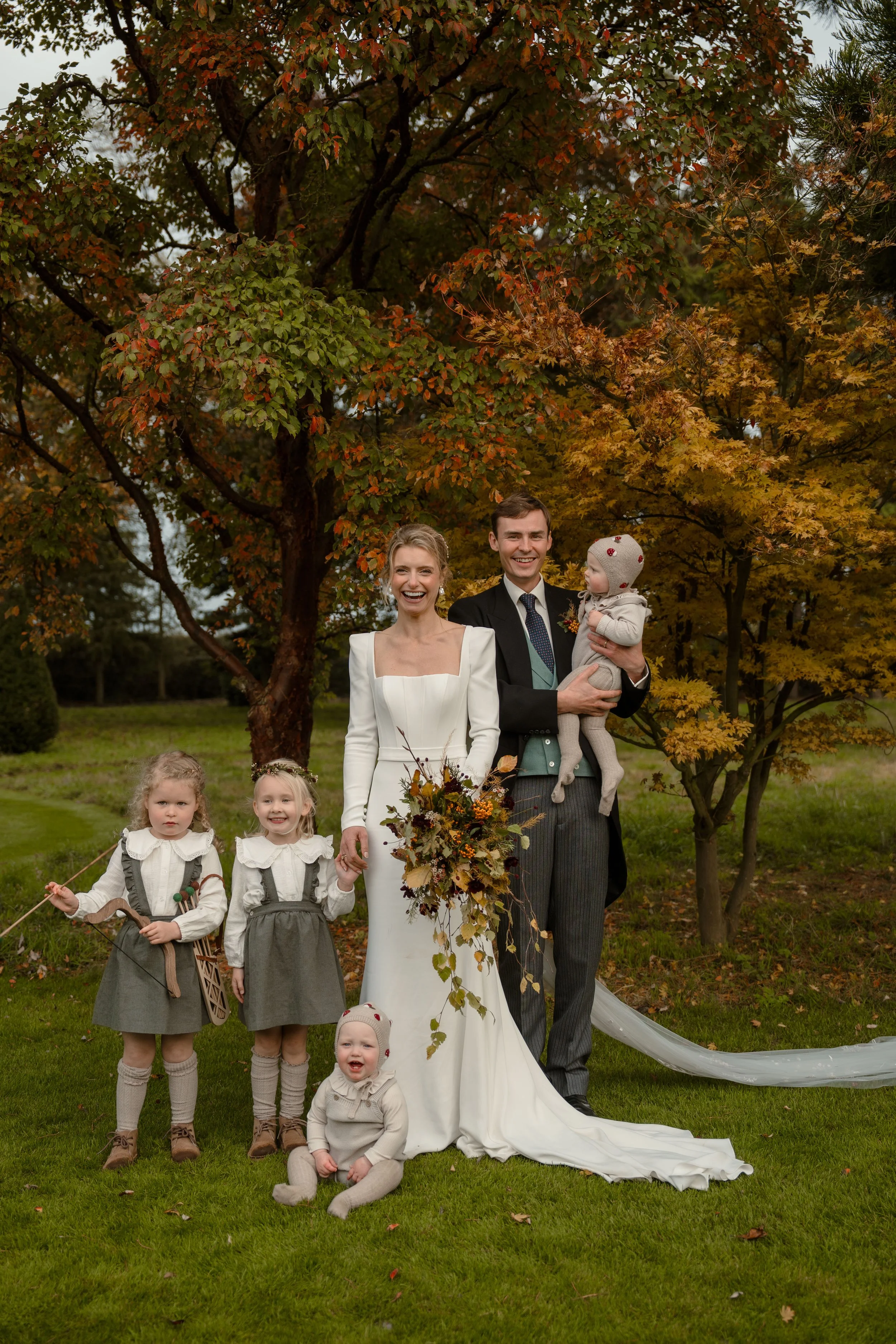 Bride and groom with parents and children in an outdoor family group photo at a wedding ceremony venue.