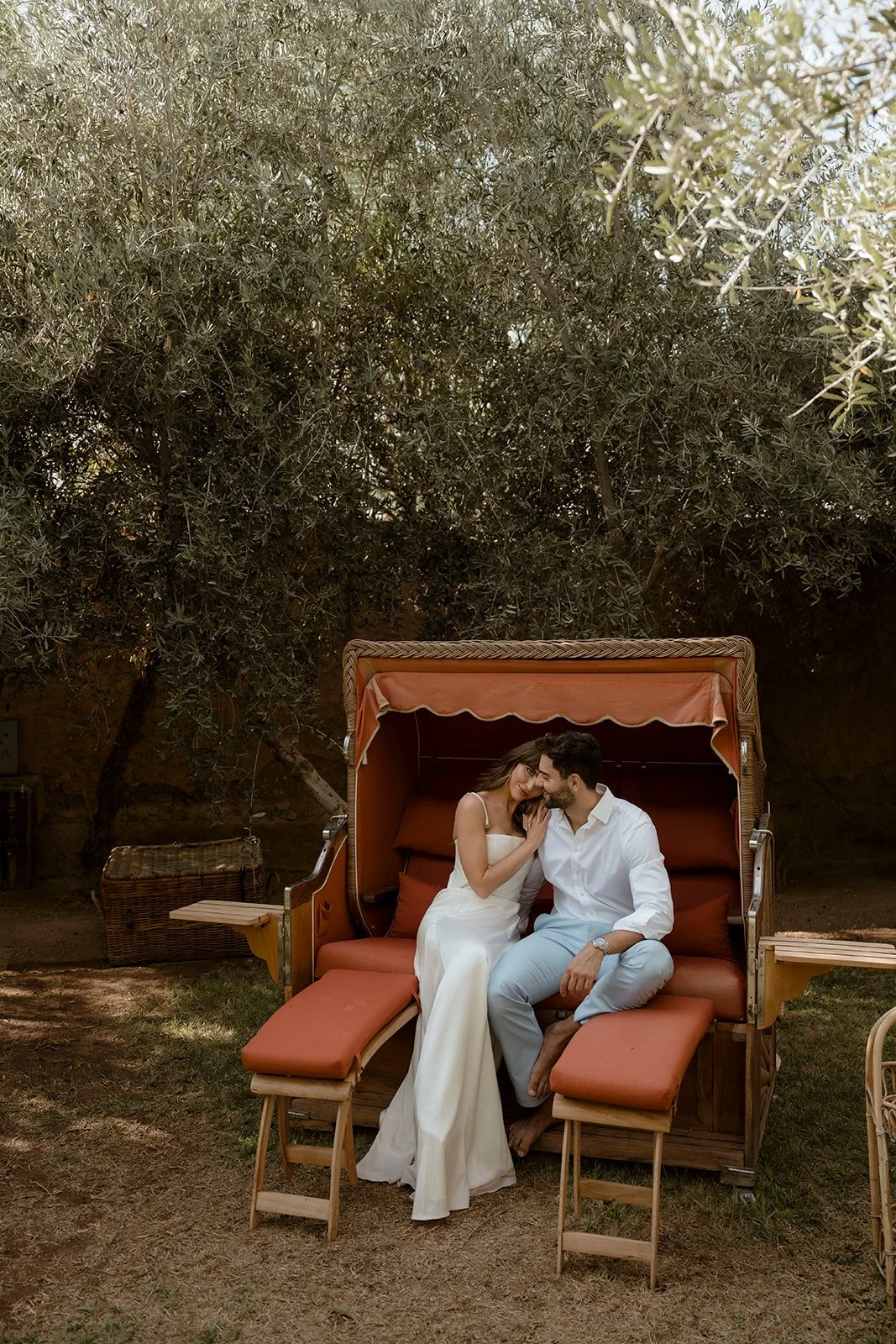Bride and groom sitting together on an outdoor daybed beneath olive trees in the garden at Hotel Les Deux Tours, Marrakech.