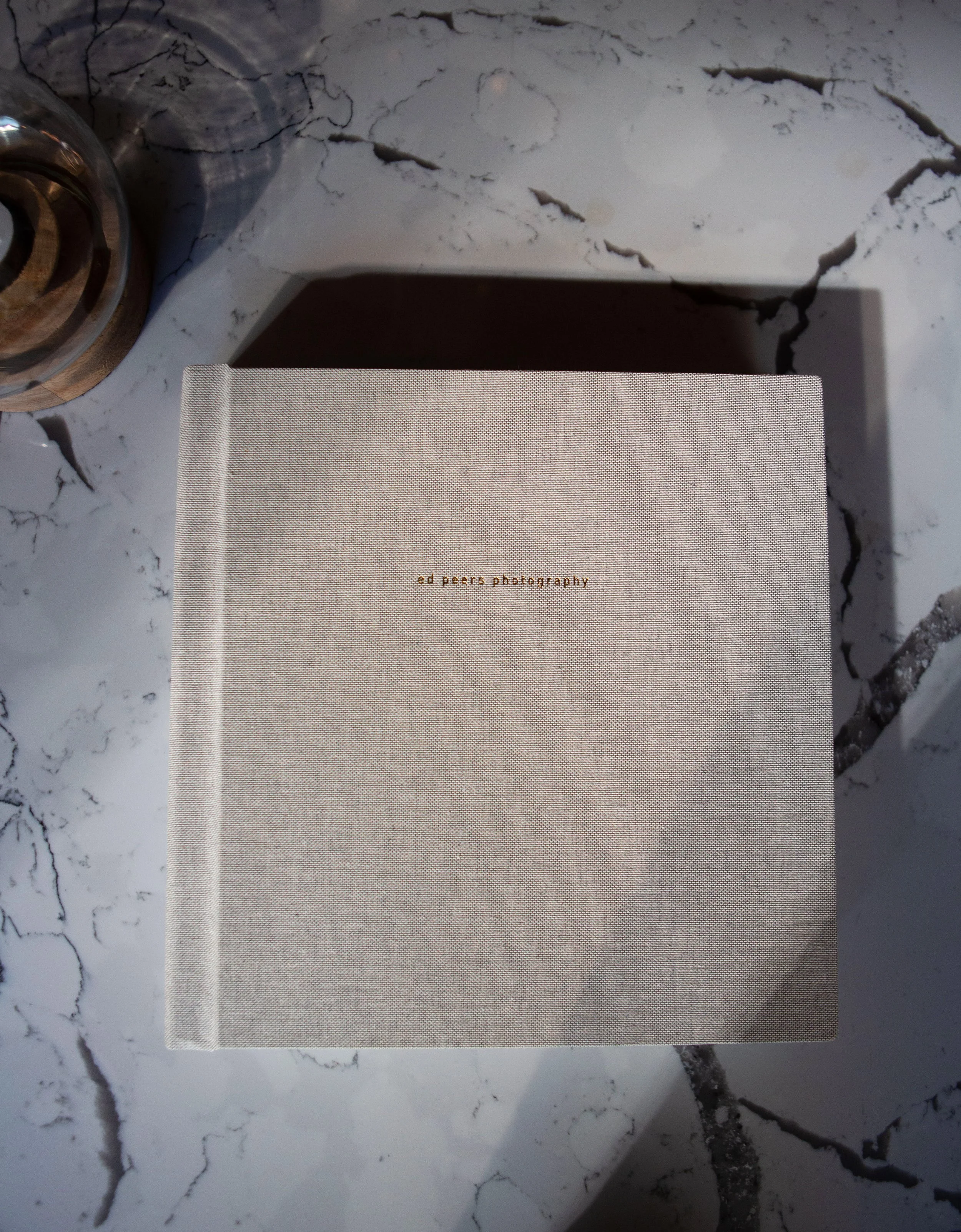 Square linen wedding album with embossed cover placed on a marble surface.