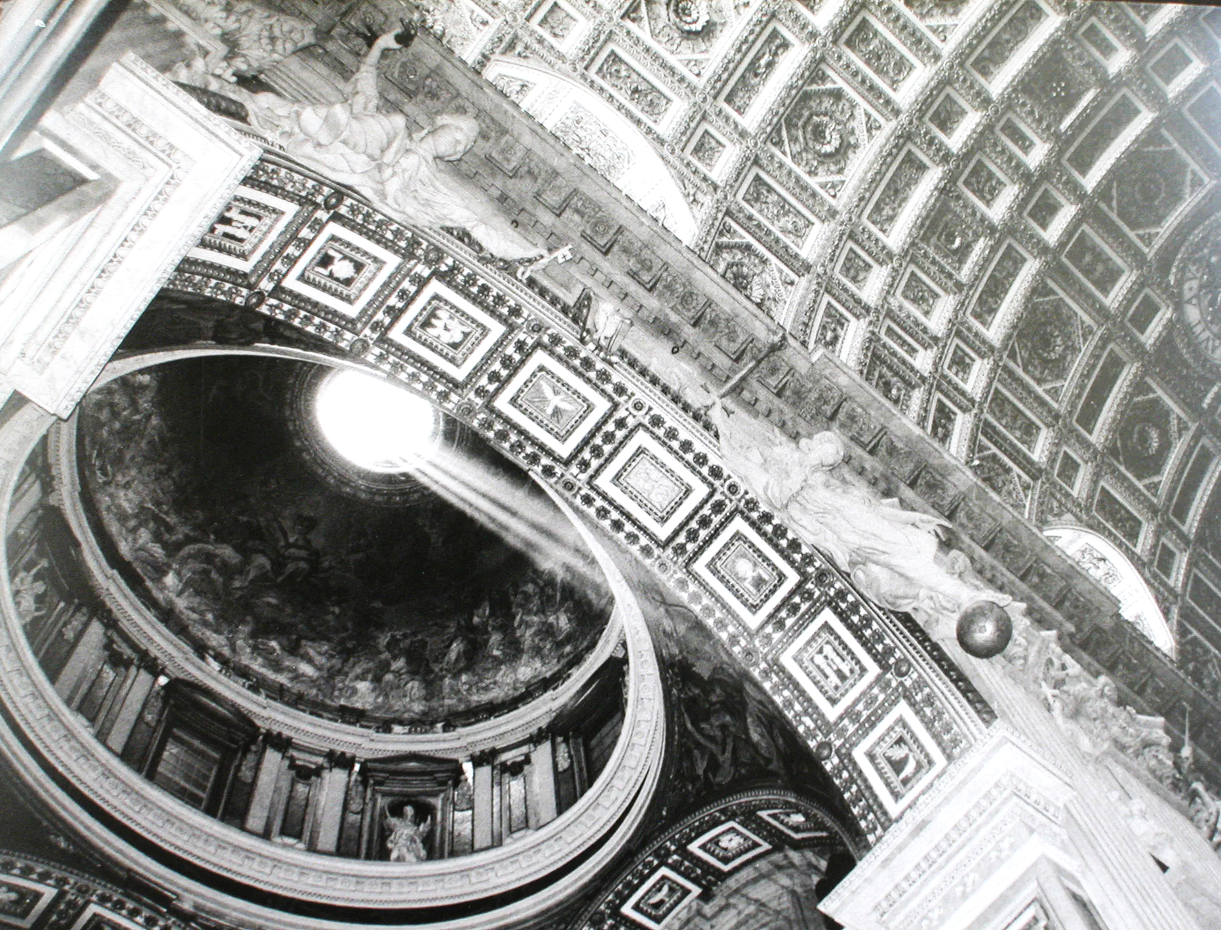 Looking upward at an ornate decorated ceiling with detailed patterns and sculptures, featuring a circular opening with a bright light shining through.