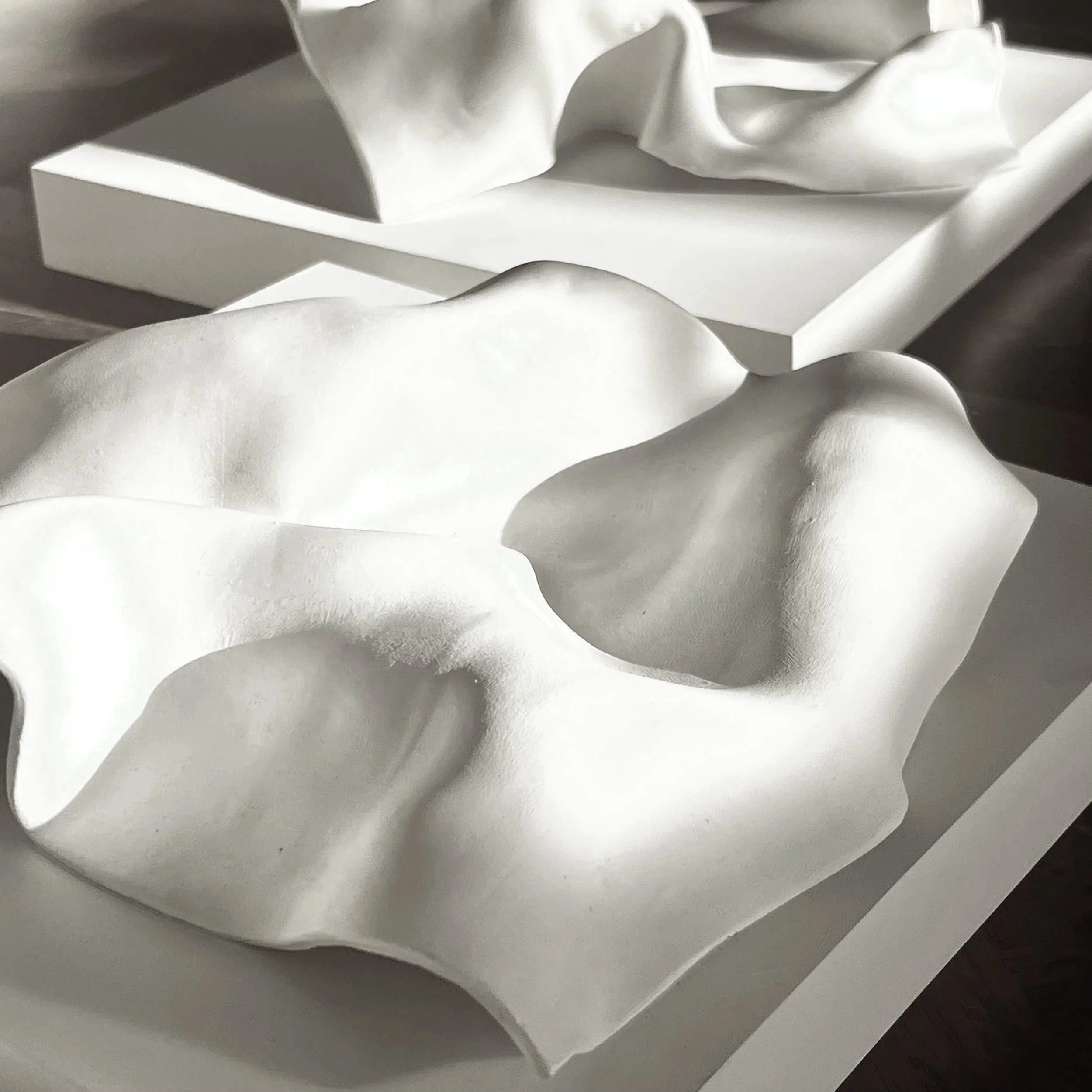a modern abstract art piece. Close-up of a detailed white ceramic or porcelain sculpture with flowing, organic shapes and smooth surfaces,  resembling a fluid handkerchief.