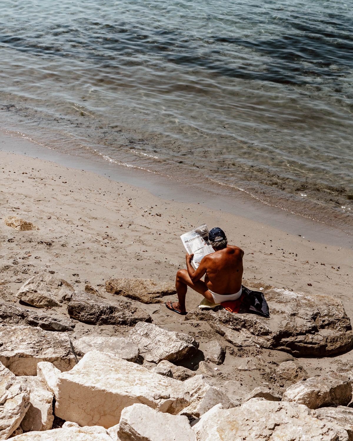 Man reading newspaper on beach, Sicily