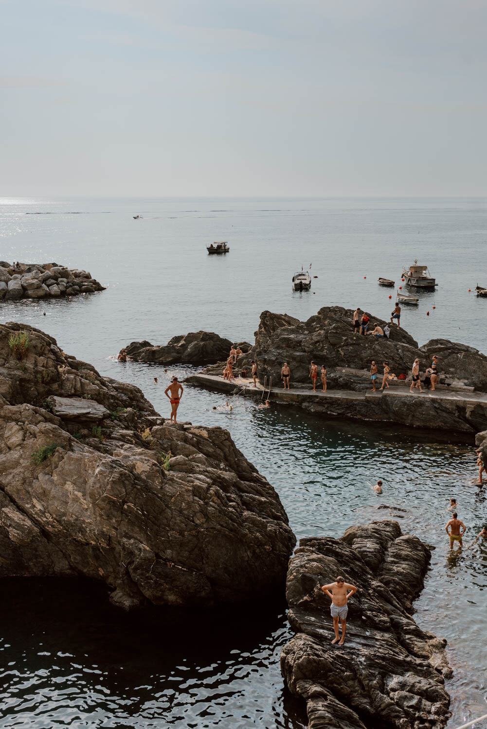 people swimming, sunbathing and standing in manarola harbour
