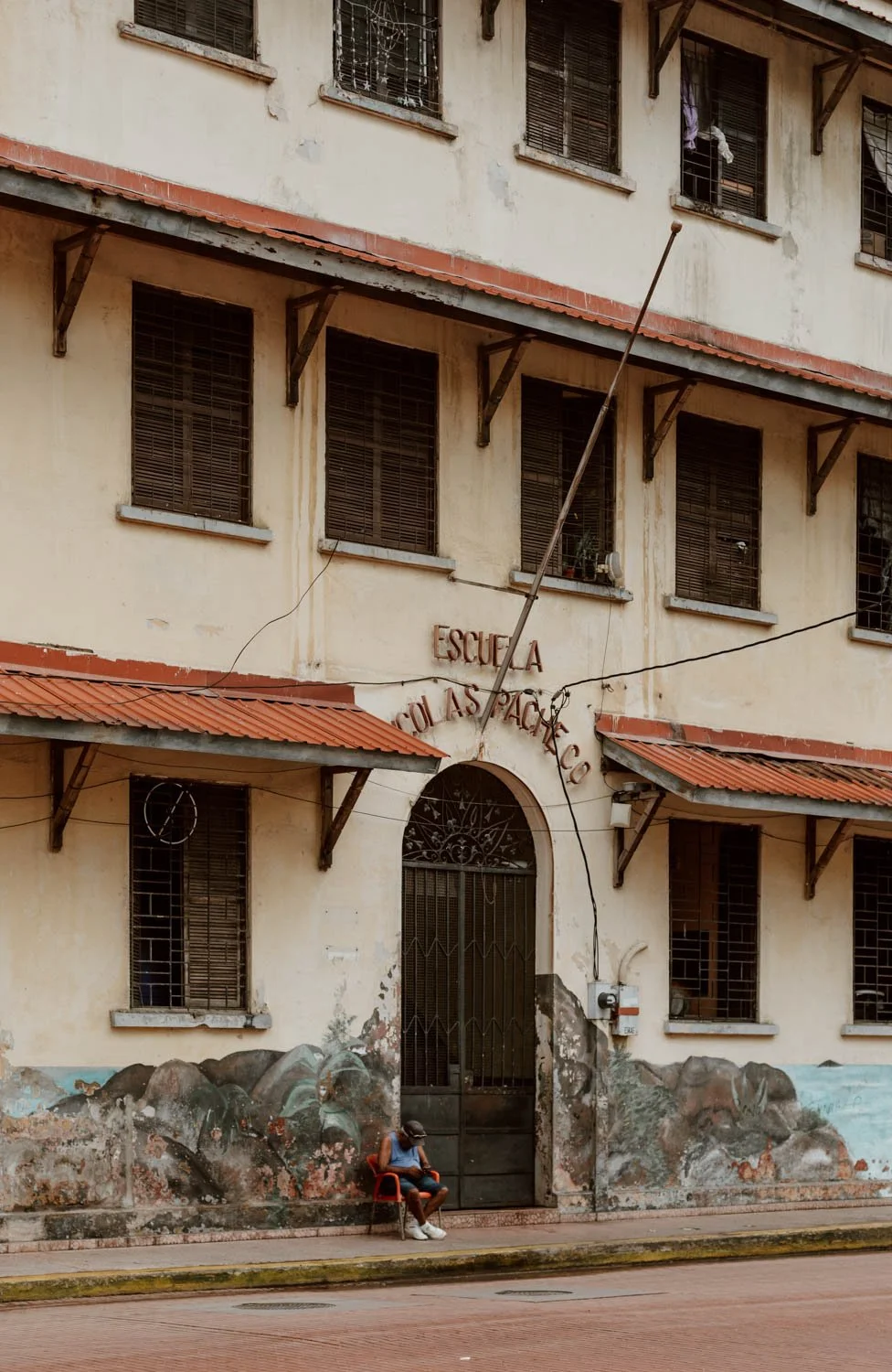 man sits on chair in front of school in casco viejo, panama city