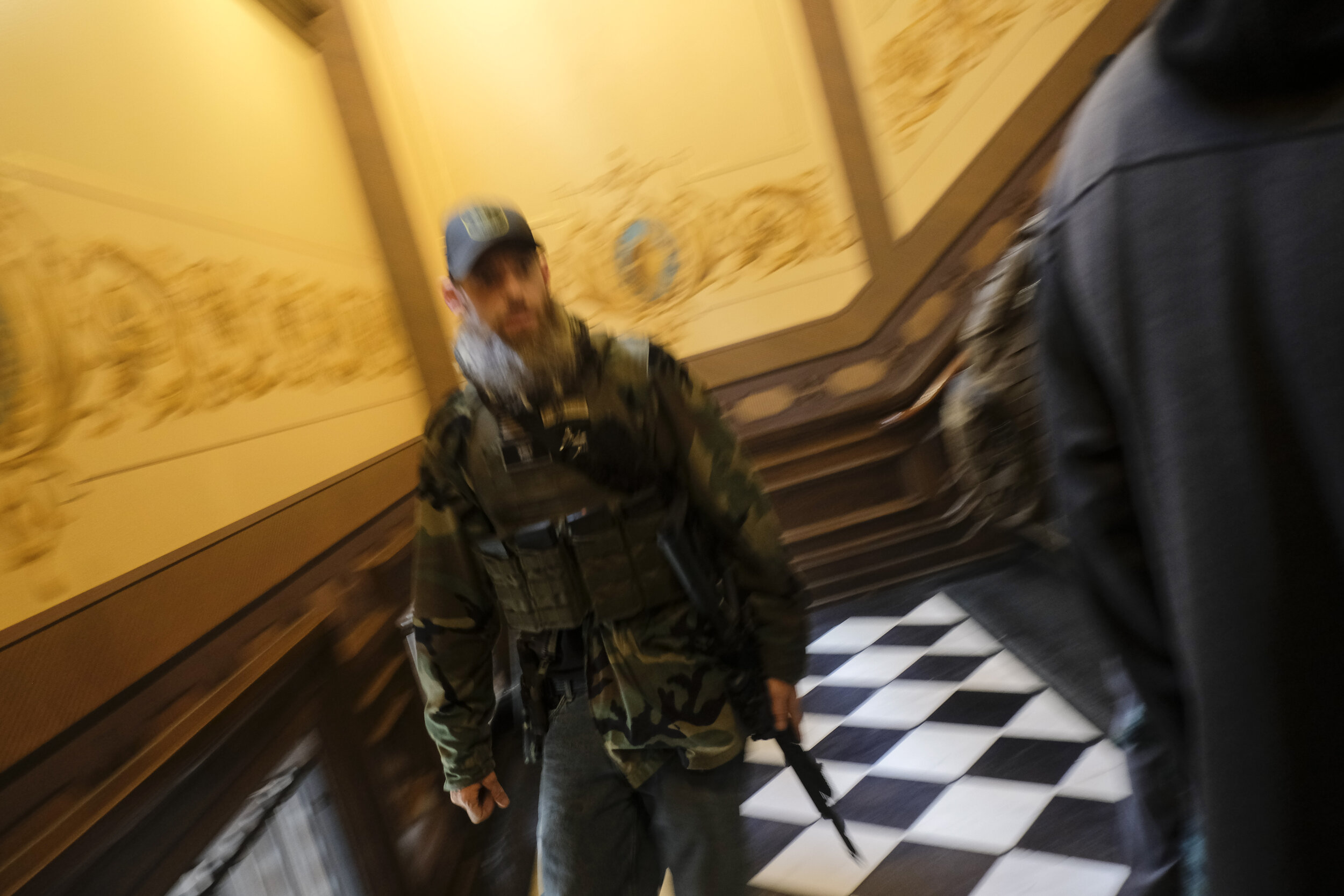  An armed member of a Michigan militia runs down the stairs shouting at police officers near the senate chamber of the Michigan Capitol Building in Lansing, Michigan on Thursday, April 30. After Michigan Governor Gretchen Whitmer announced she would 