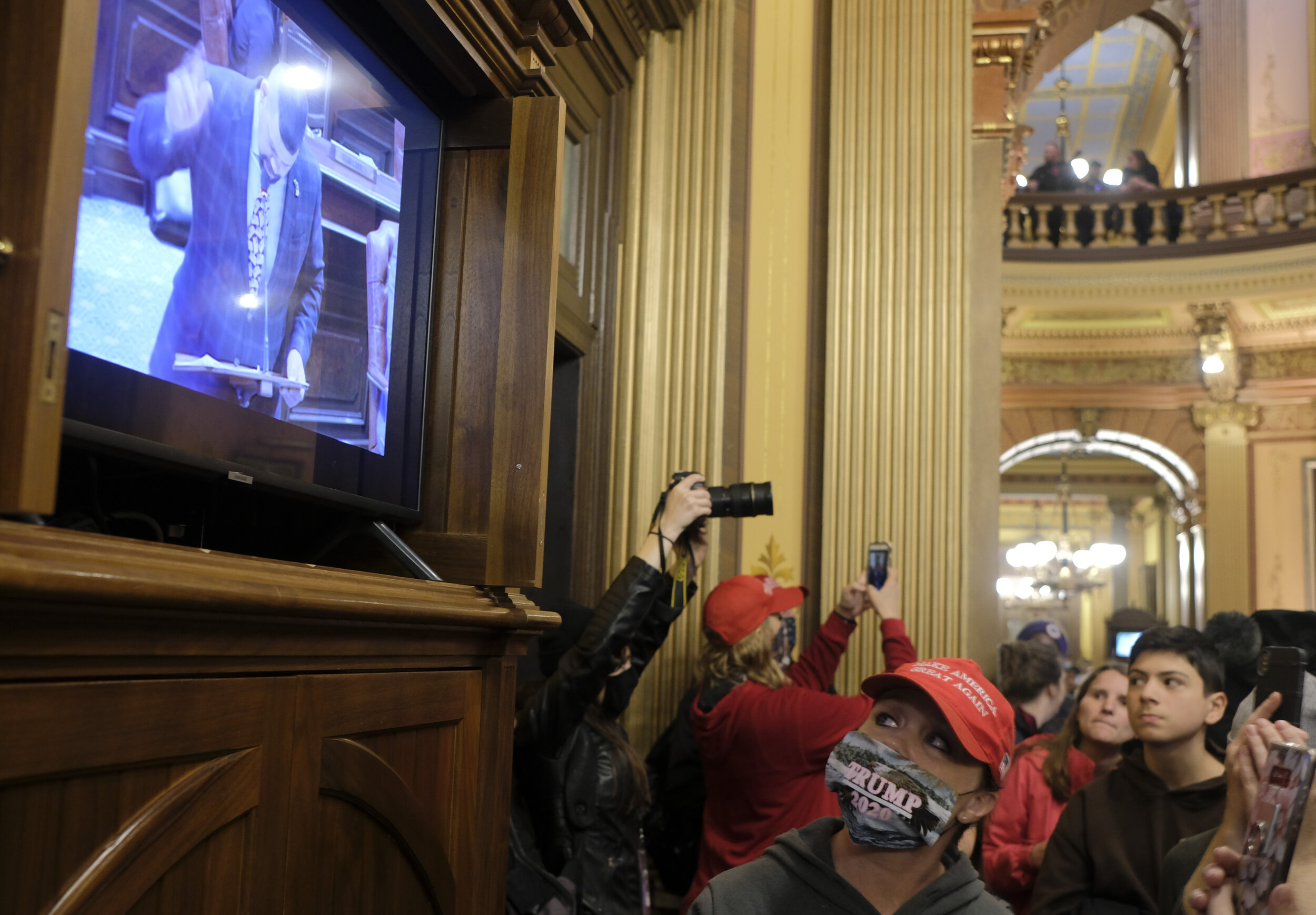  An anti-lockdown protester watches the senate meeting underway on a television in the Michigan Capitol Building during a large anti-lockdown protest during which armed protesters and militia members occupied the area just outside the Senate chamber 