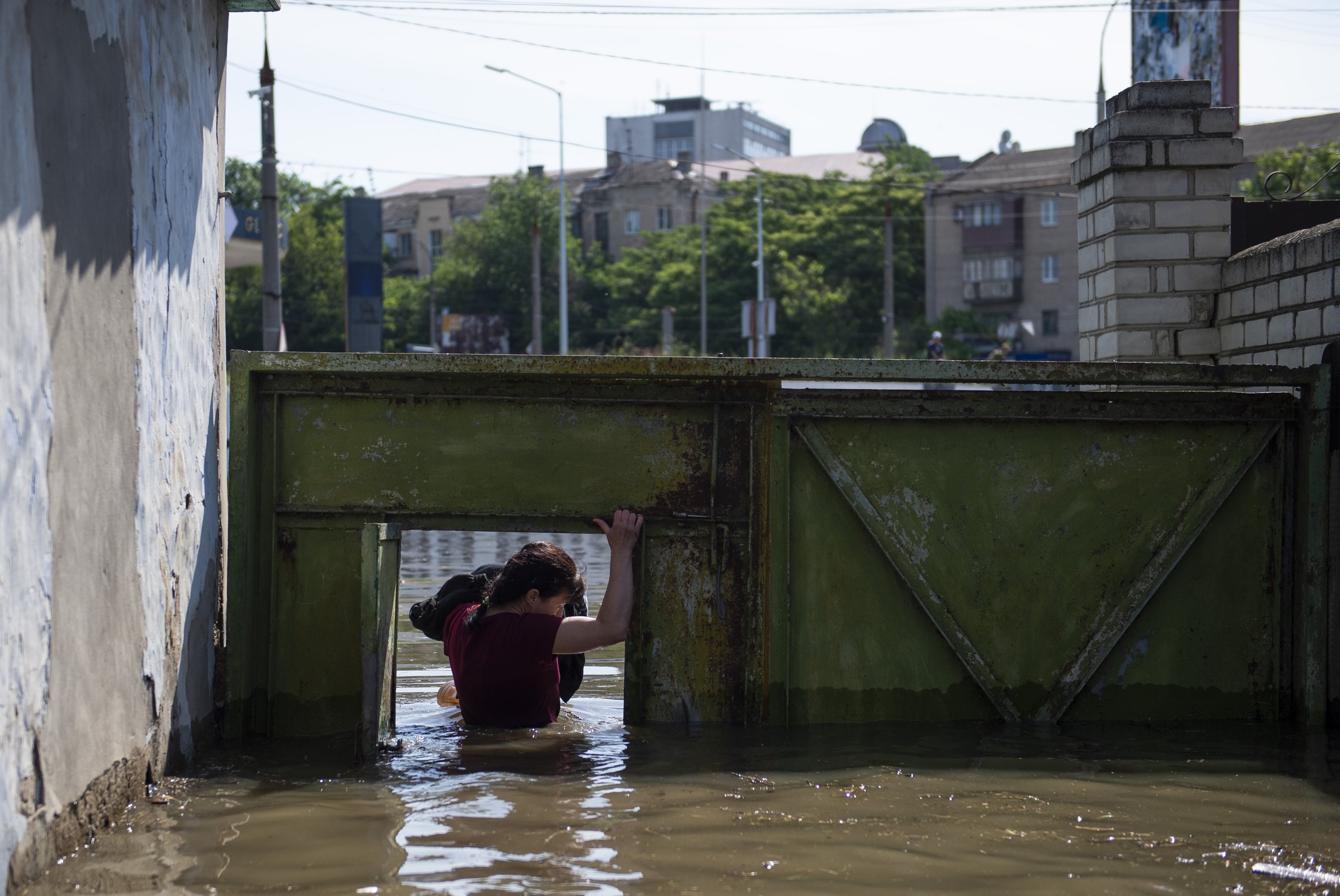  A woman ducks under a doorway as she wades through floodwaters in her neighborhood near the Dnipro River in Kherson, Ukraine on June 7, 2023. Russian forces destroyed the Kharkovka Dam which flooded communities along the Dnipro River.   