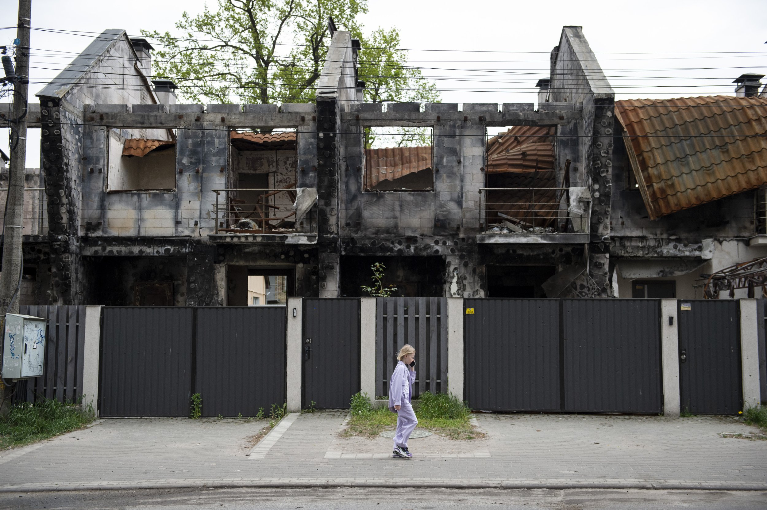  A young girl talks on her cell phone as she walks past a row of buildings bearing the scars of the heavy fighting that occured  one year earlier in Irpin, Ukraine on May 18, 2023. 