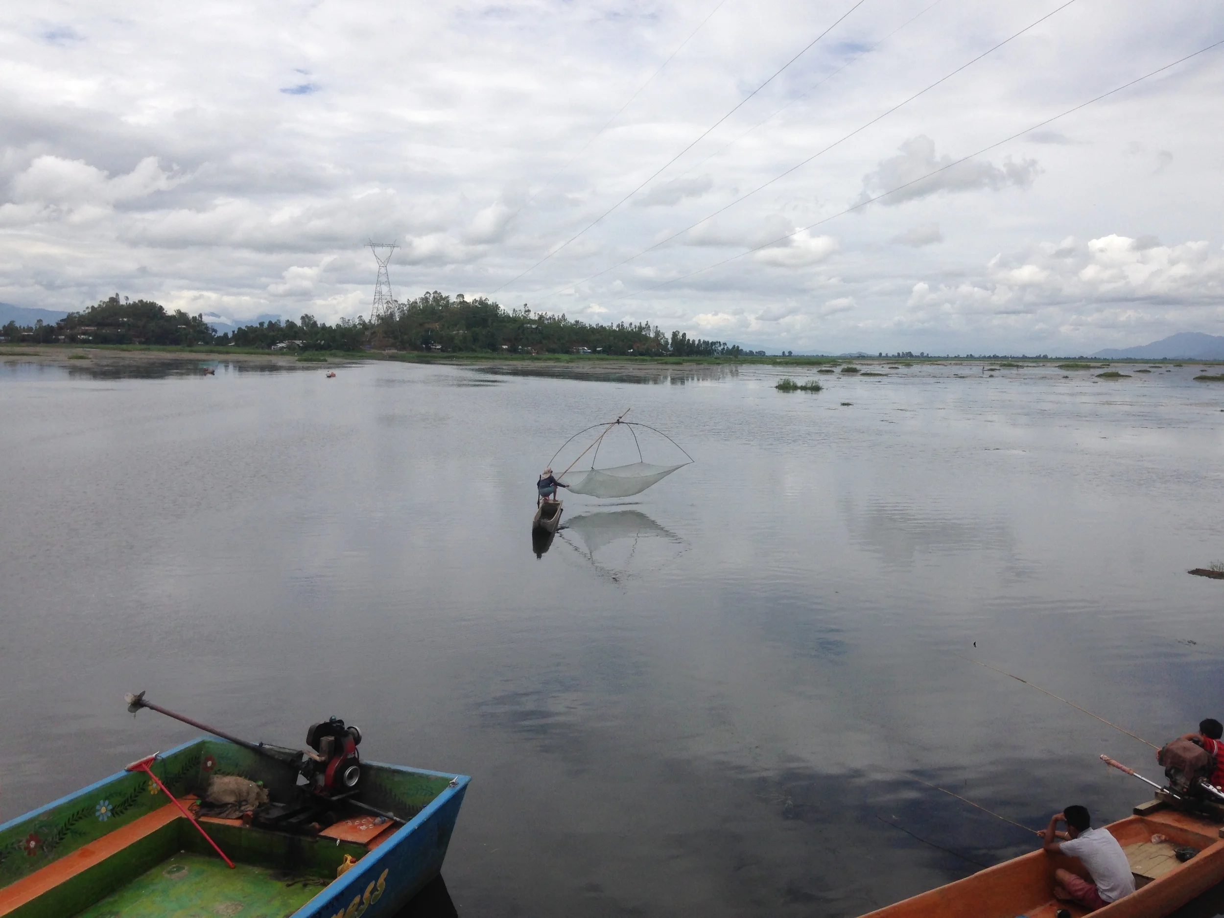 A woman fishing by controlling the net between her legs and balancing on the edge of the boat the on the lake.