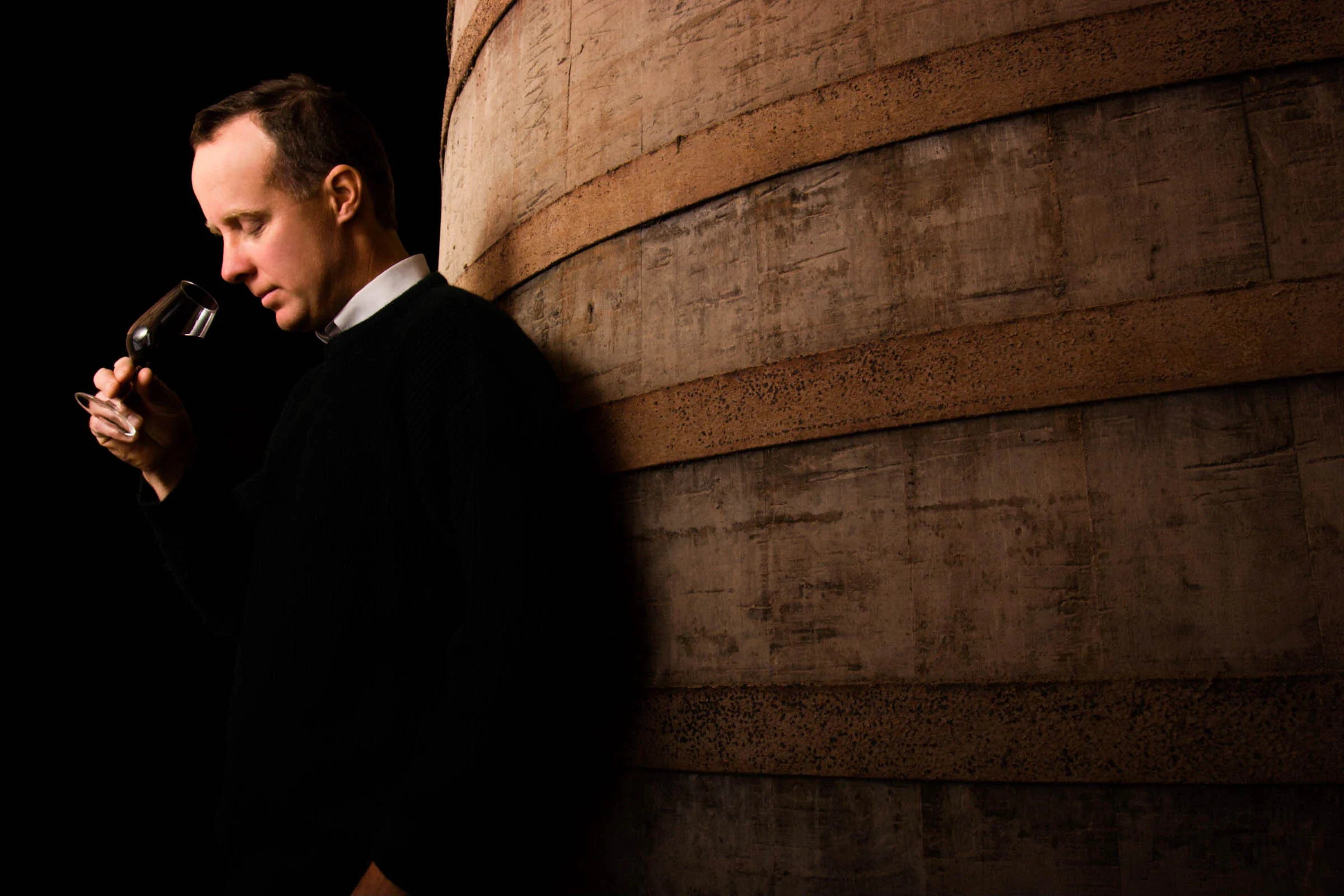  Man standing next to barrel of wine smells red wine at winery in Yarra Valley, Victoria, Australia. 