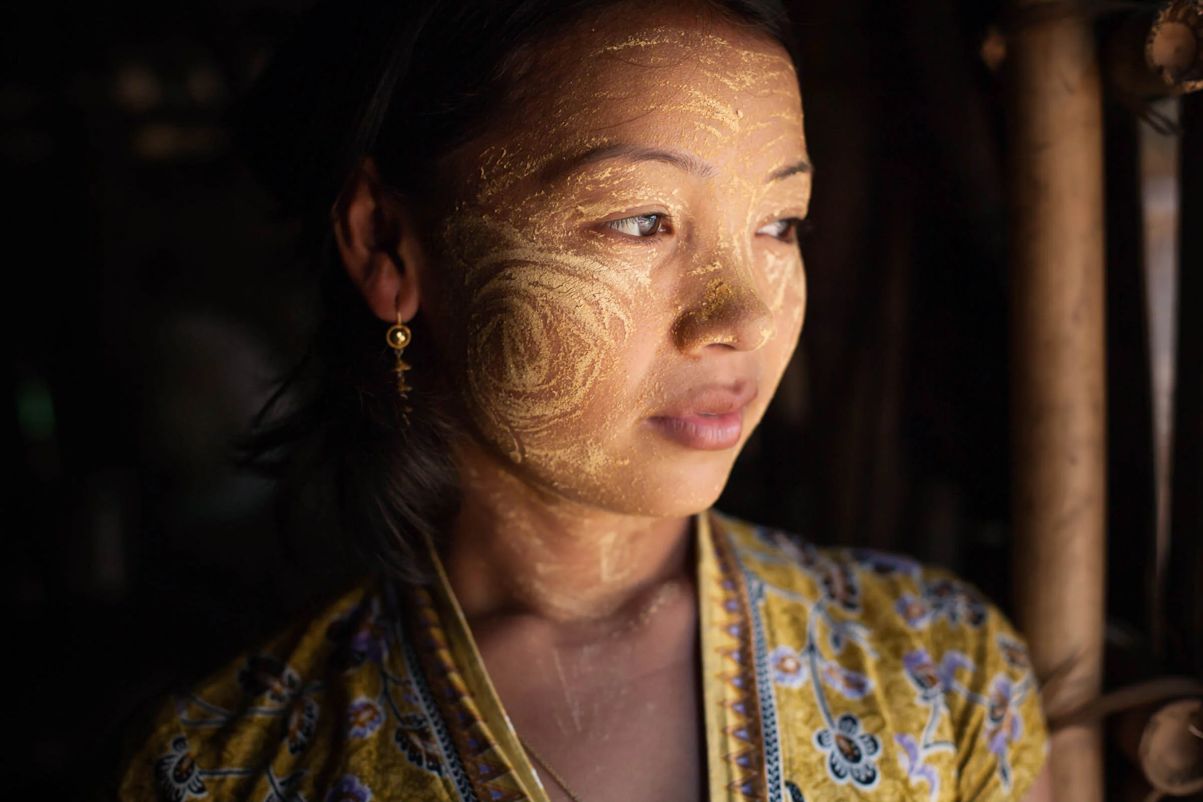 Portrait of Burmese woman looking out doorway with Thanaka paste on her face. 