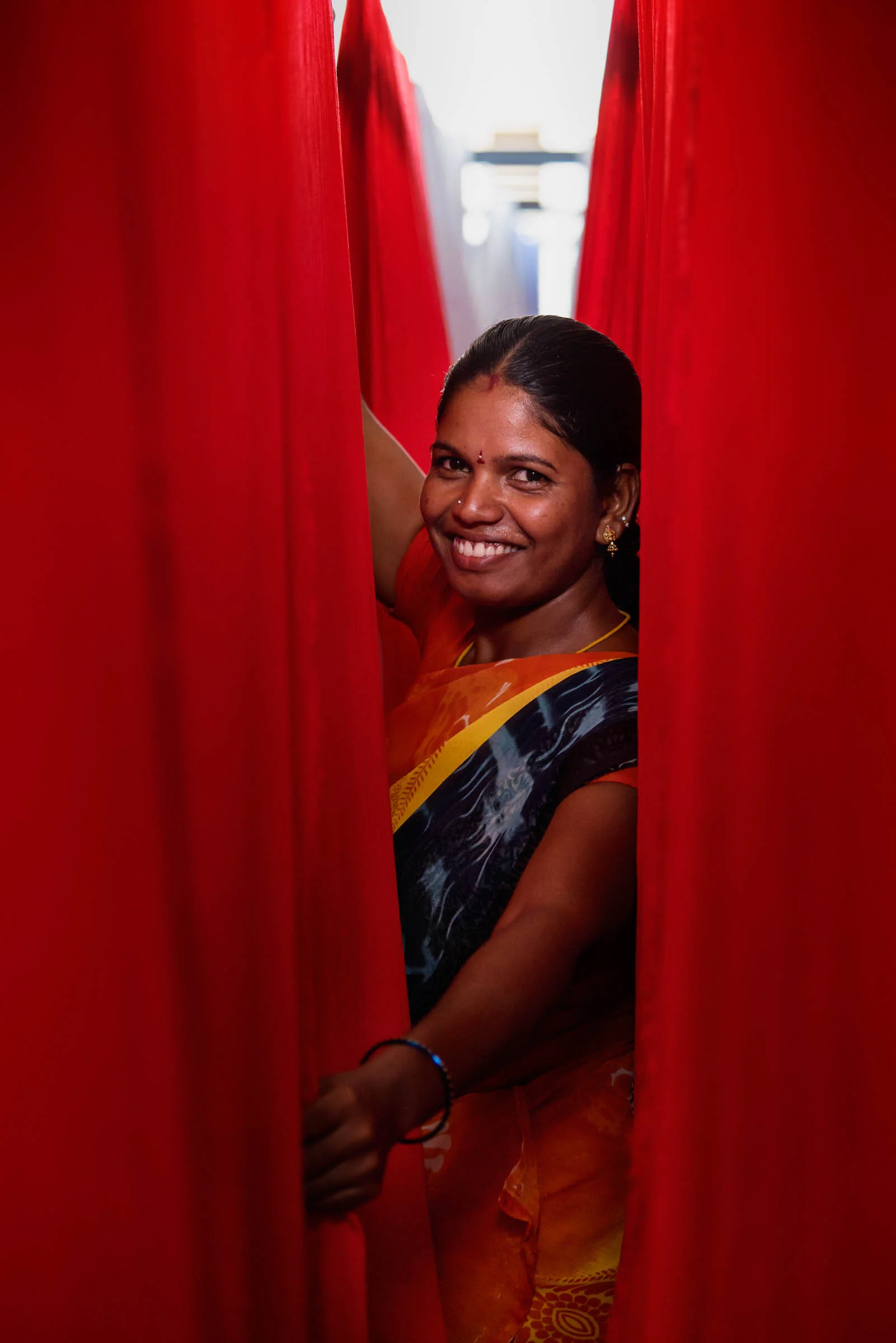  Portrait of Indian woman hanging red fabric at textile factory. 