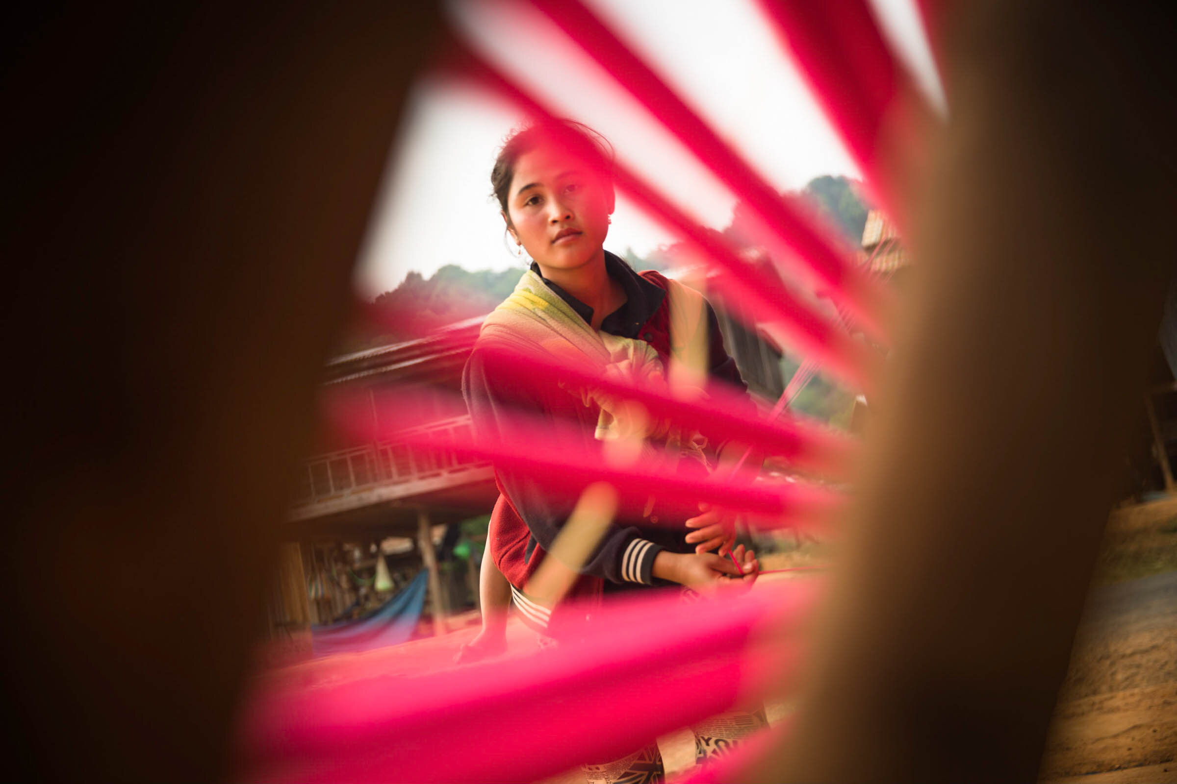  A young mother with baby on her back sorting threads, Ban Nakout, Laos. 