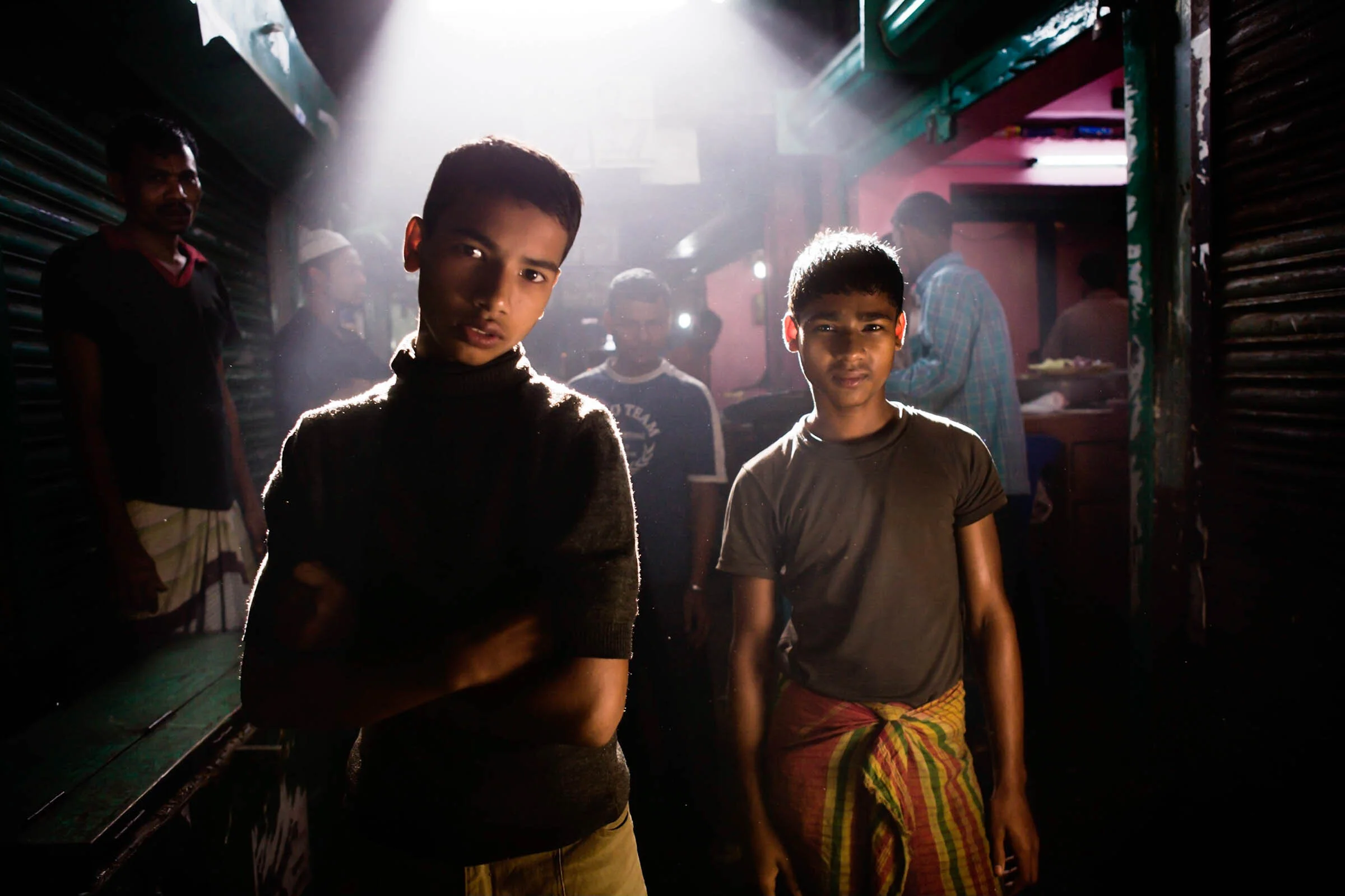  Two young boys at the Nawabganj Bazar are backlit as the sun breaks through the market roof, Rangpur, Bangladesh. 