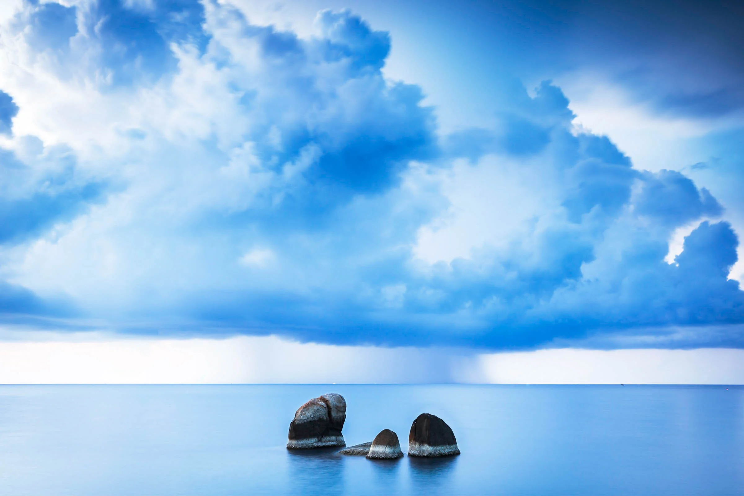  Rocks and calm seas as a storm passes in the distance, Ko Samui, Thailand. 