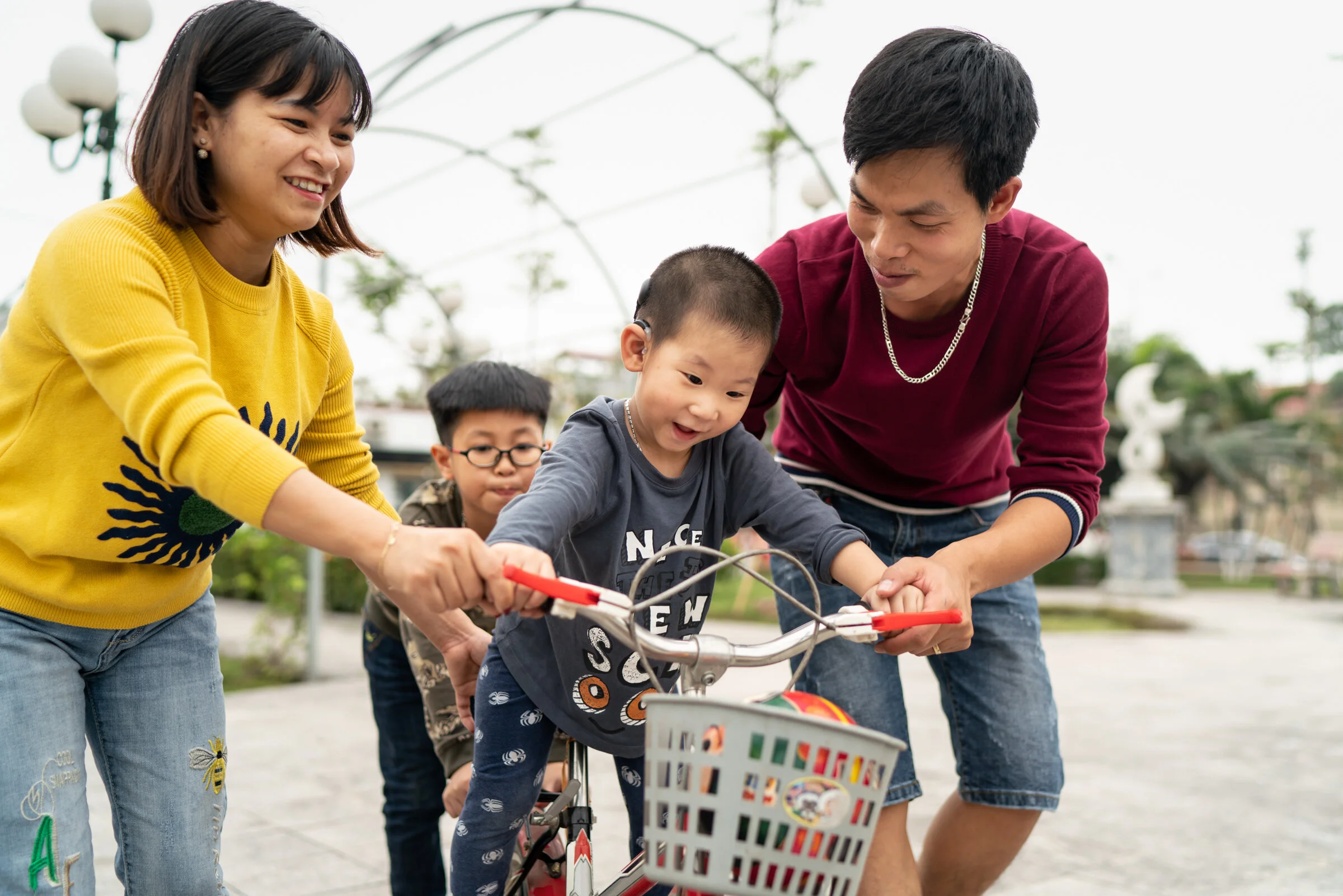  Young boy with Cochlear Implant rides bike as his parents and brother help him, Hanoi, Vietnam. 