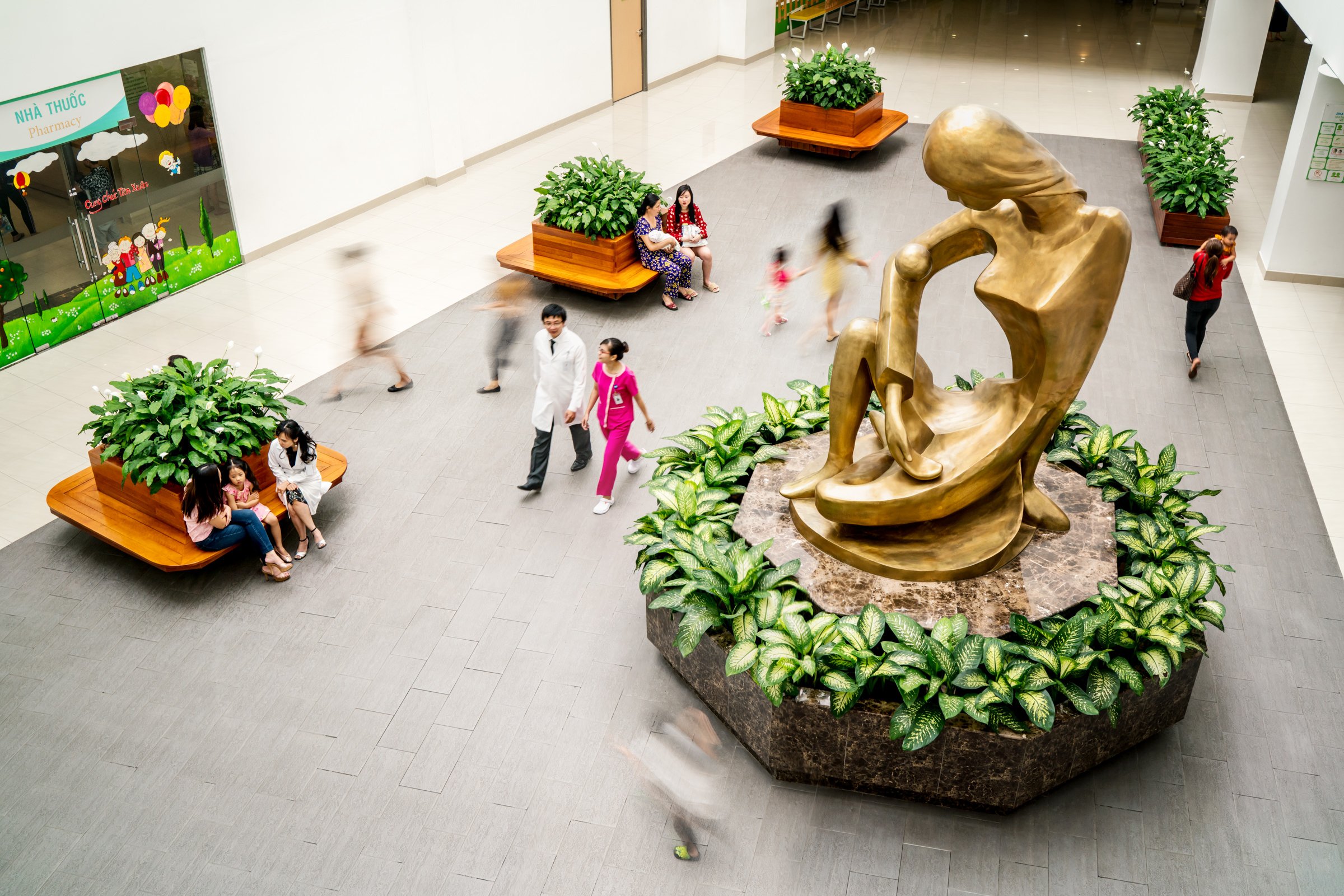 Aerial view as doctors, nurses and patients walk past maternal statue in the Hanh Phuc Hospital reception area.