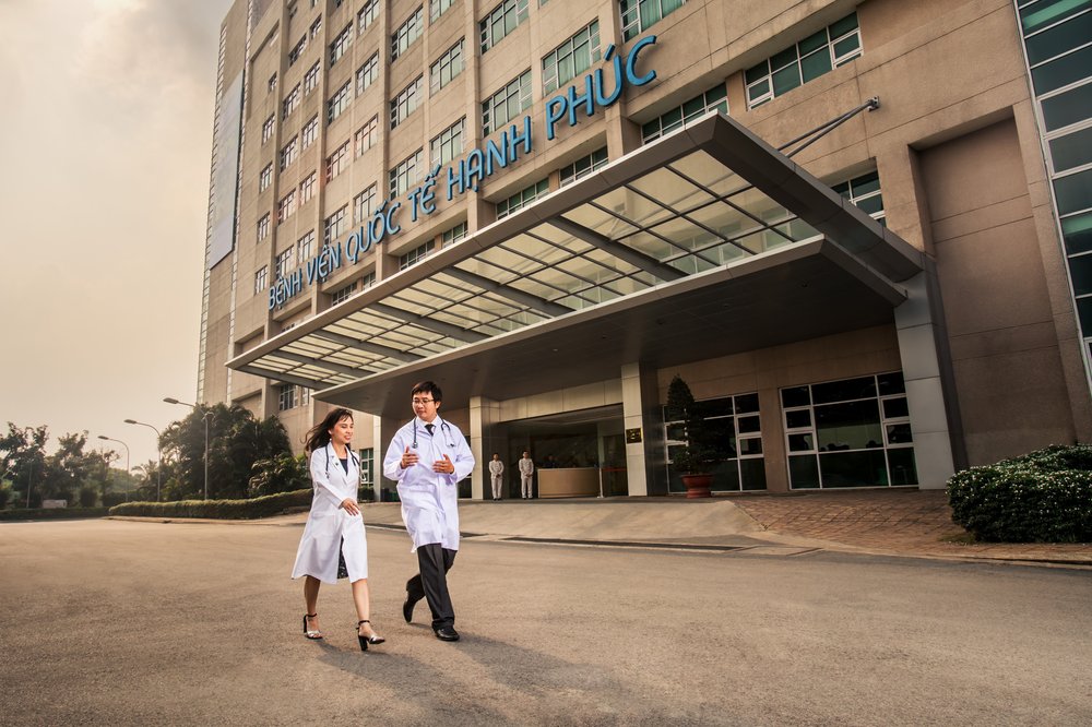 Female and Male Doctors talk as they walk outside the entrance of Hanh Phuc Hospital