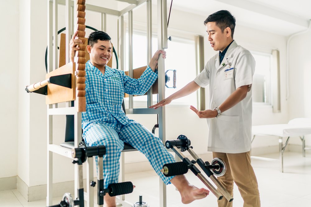 A patient does seated leg extension curls with a physiotherapist at Hoan My Saigon