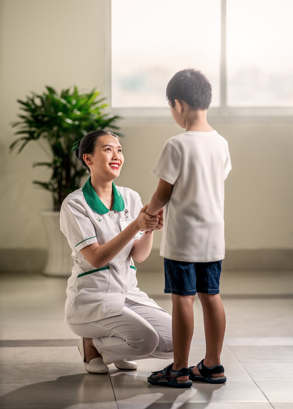 Nurse kneels down to comfort young male patient in corridor at Hoan My Saigon Hospital.