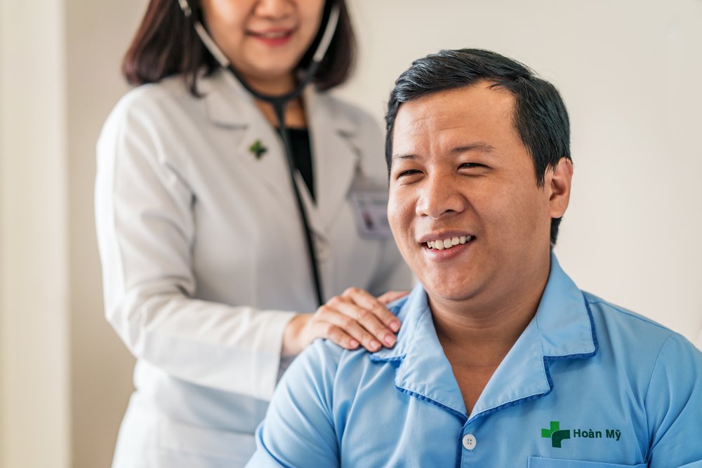 A patient smiles warmly as a female doctor check his health with stethoscope.