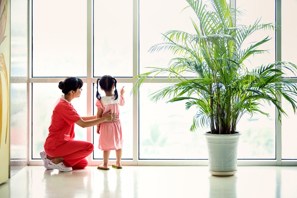 Nurse kneeling down and looking out window with young girl.