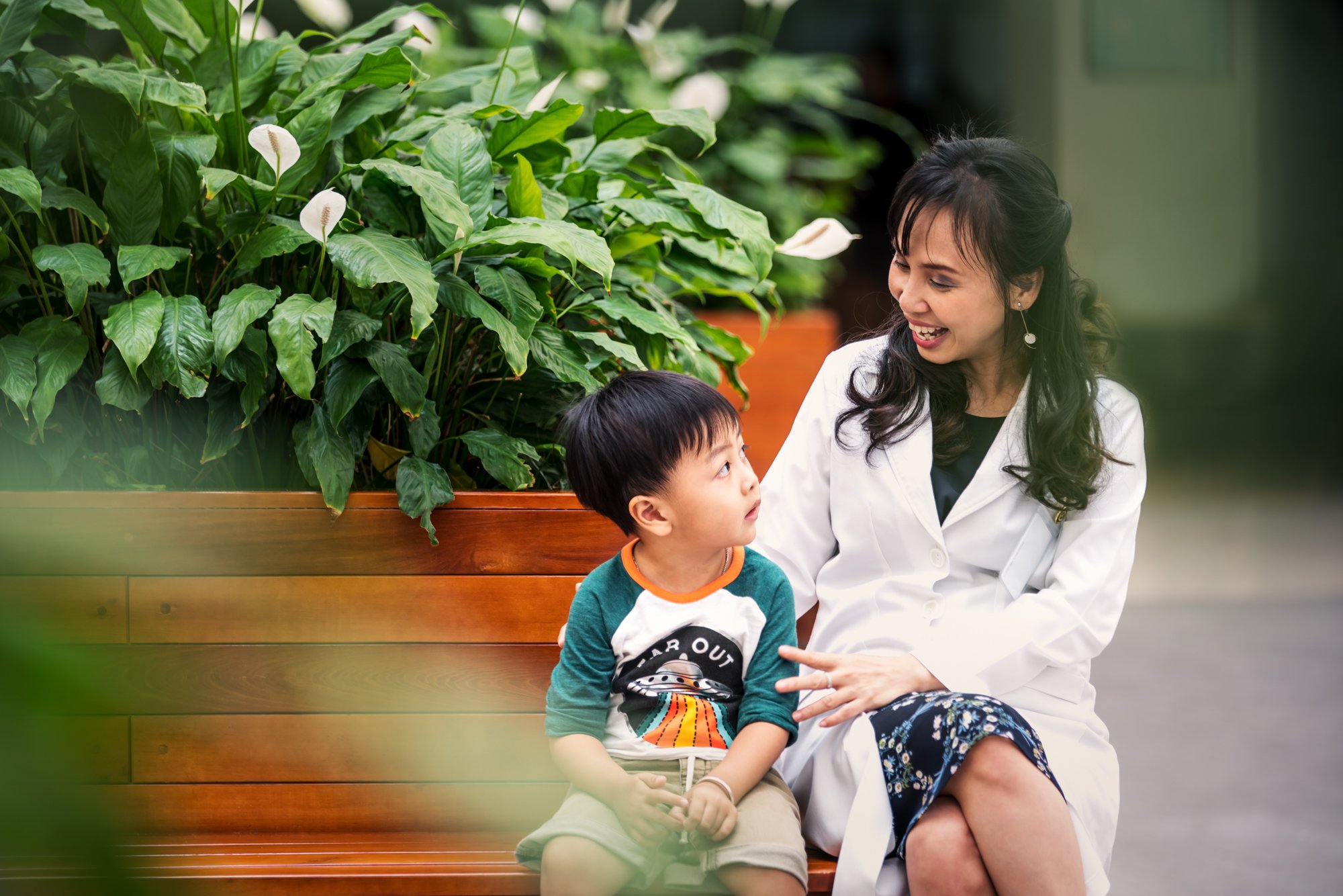 Female doctor sits with and comforts young child on a bench at Hanh Phuc International Hospital.