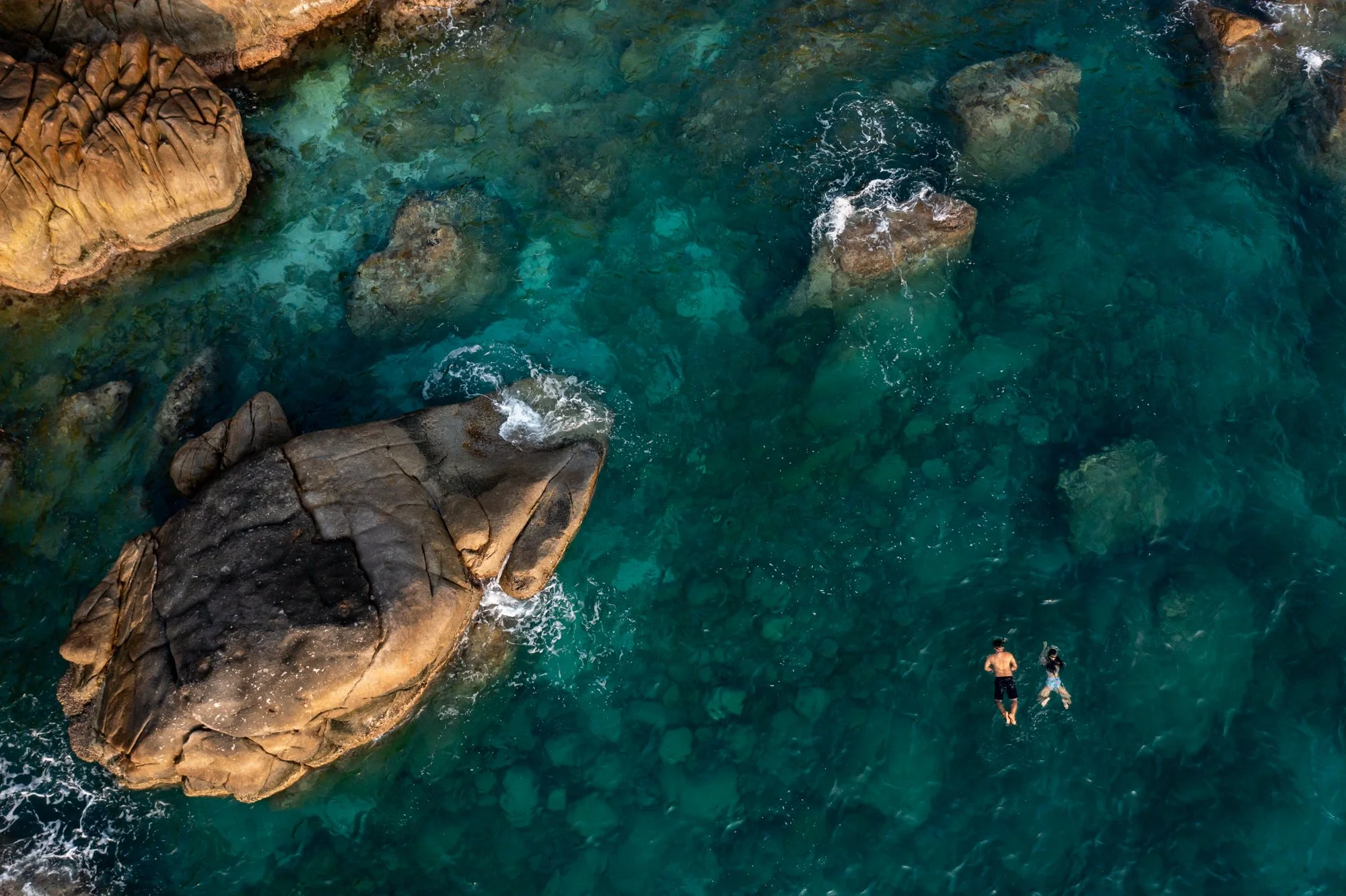  Aerial view of male and female snorkeling off rocky coastline. 