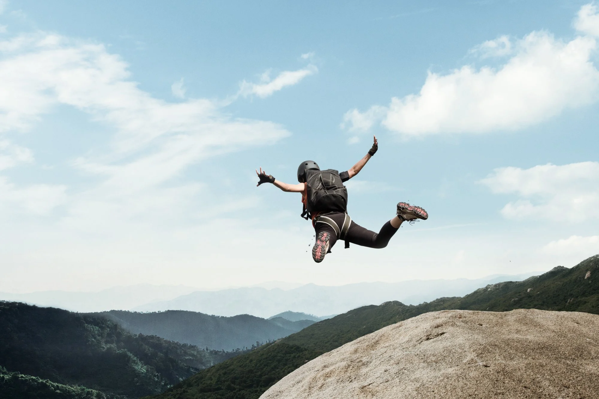  Female base jumper in mid air after cliff jump in hilly landscape. 