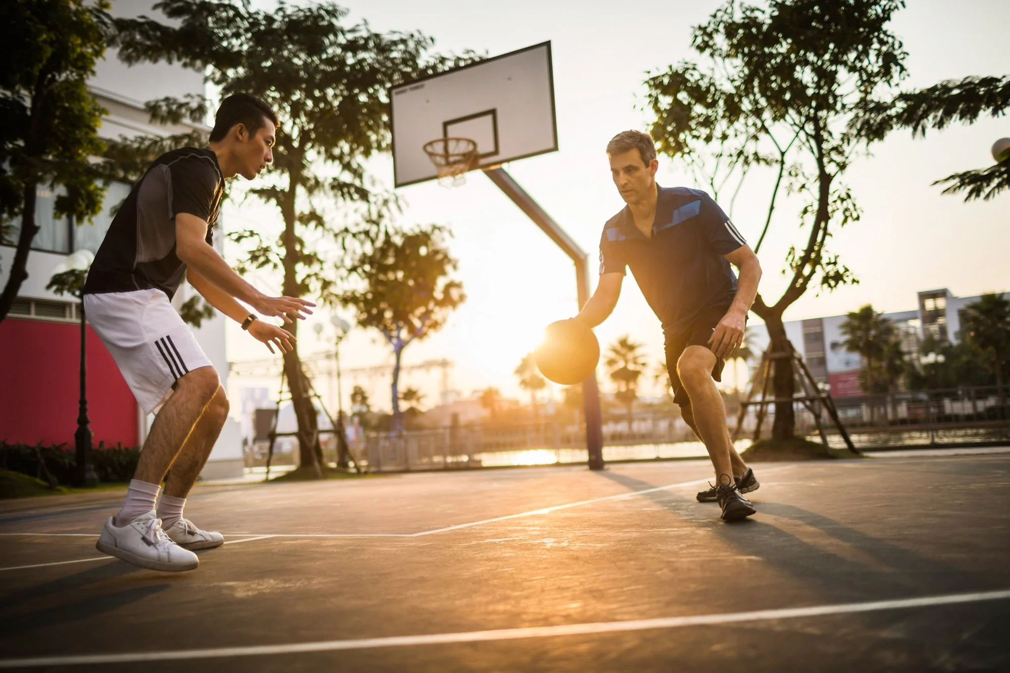  Asian and western men play basketball outdoors at sunset. 