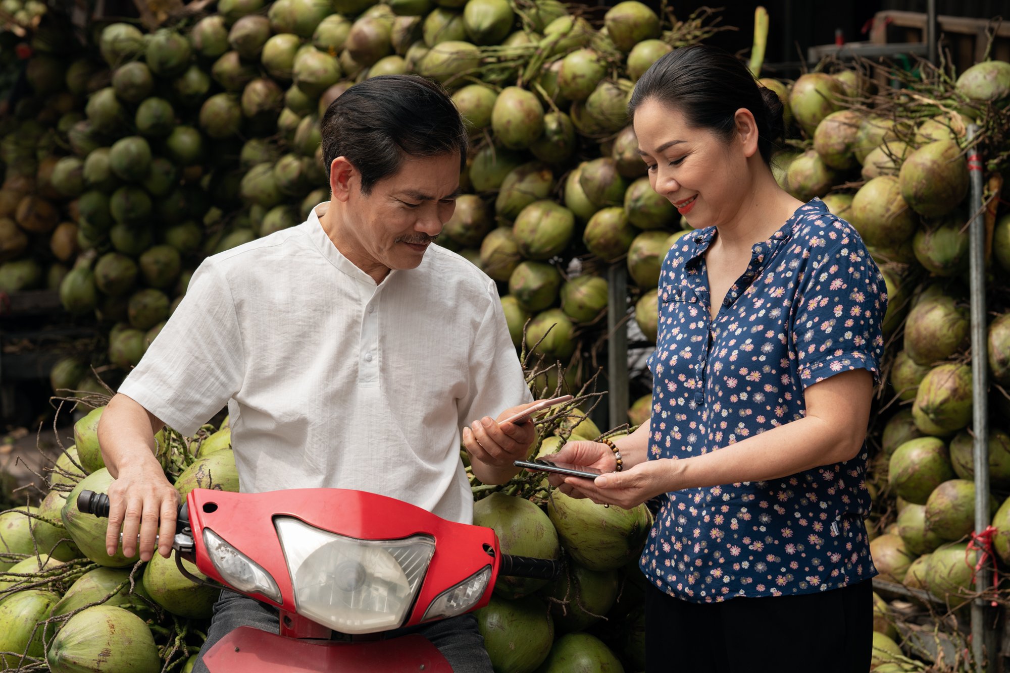  Male buyer makes payment to female seller for cocunuts with phone to phone transaction at wholsale market. 