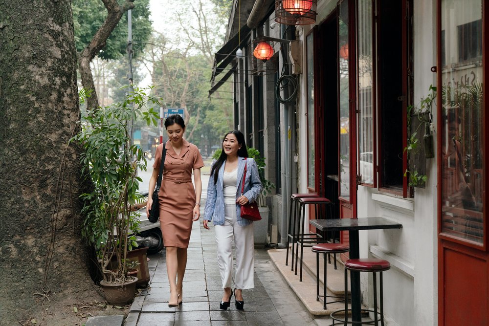  Two female financial professionals walk and talk outside artistic cafe. 