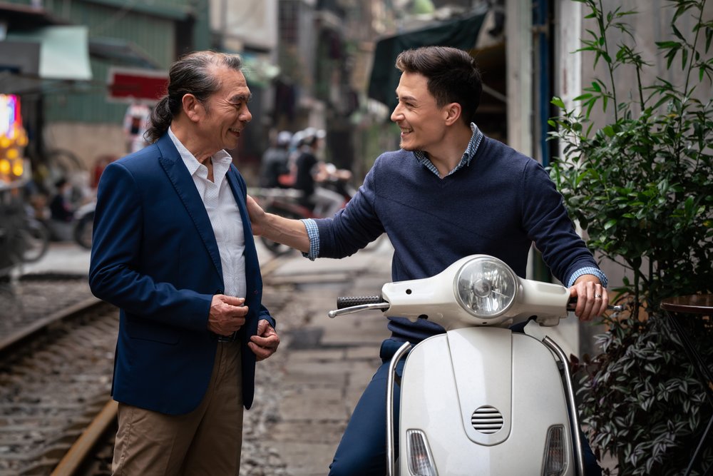  Western entrepreneur and Vietnamese businessman on motorbike greet along train tracks in Hanoi. 