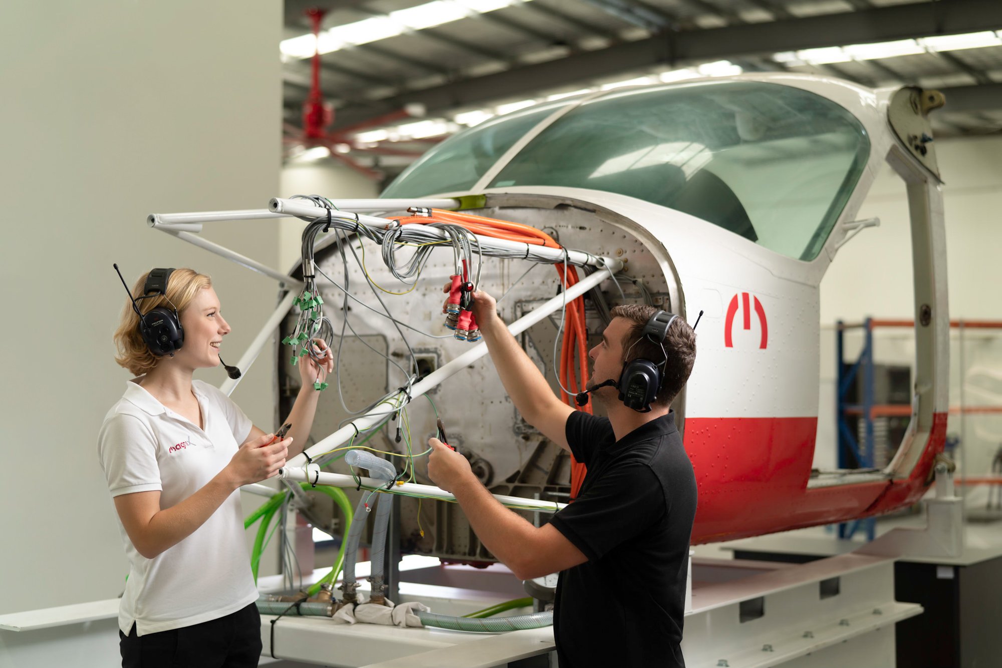  Female and male MagniX engineers check wiring on a airplane chasis. 