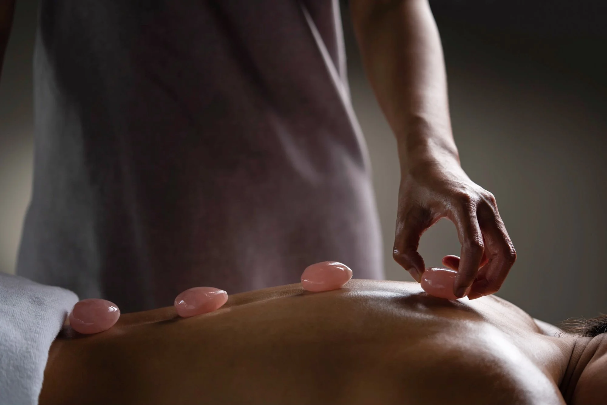  Hot stone asian therapy massage as therapist places pink stones on the back of relaxed female. 