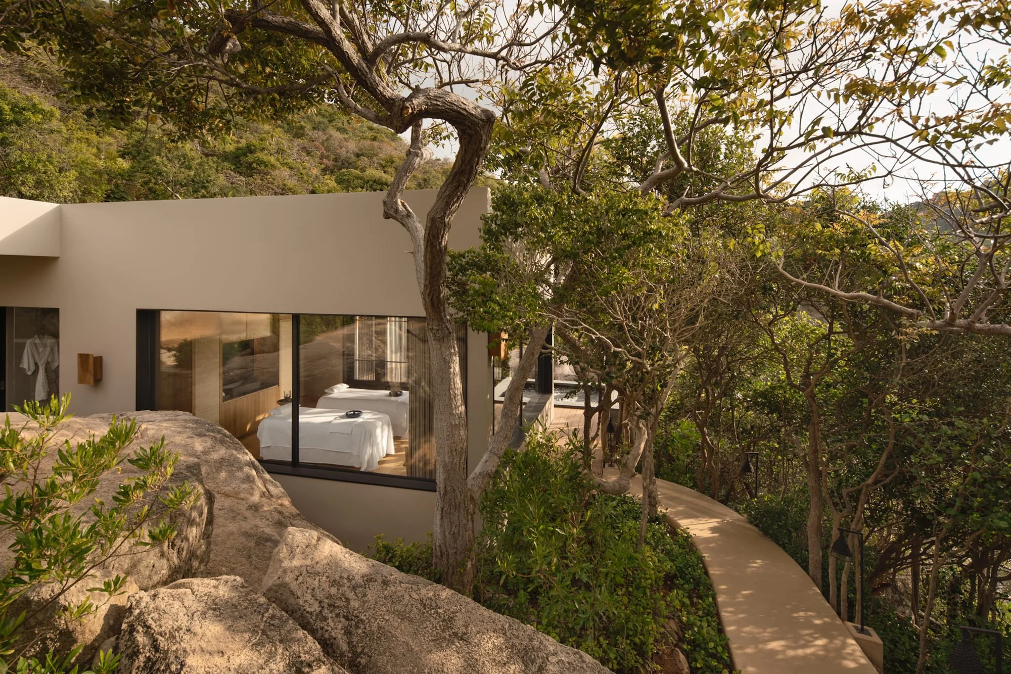  Amanoi Ocean Pool Residence nestled among trees and granite boulders, with a private spa house and pathway surrounded by lush forest. 