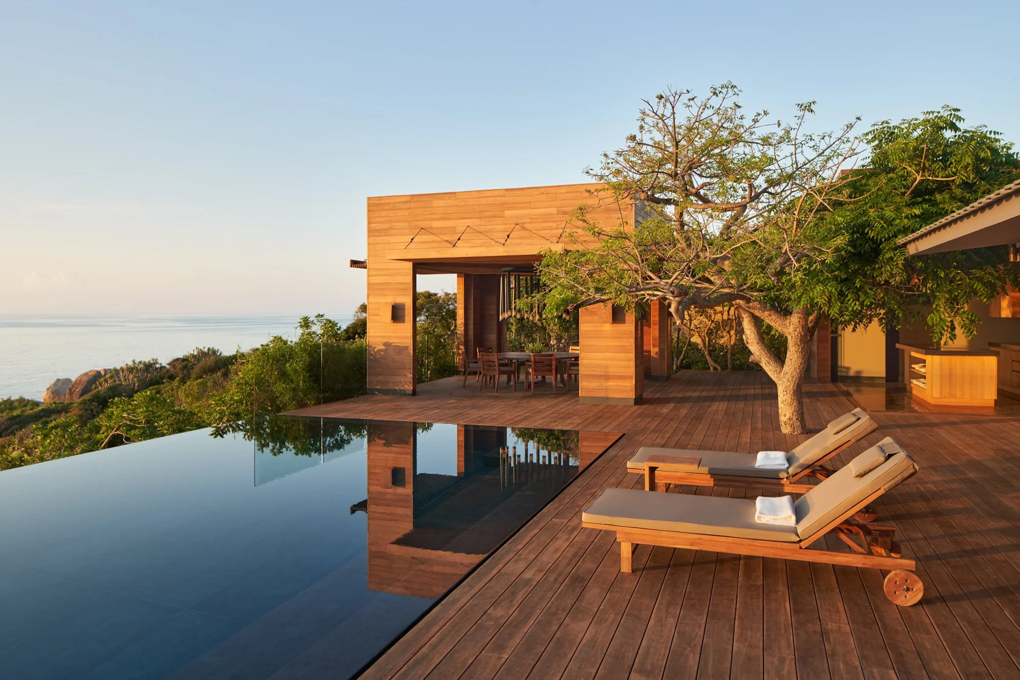  Amanoi Ocean Pool Residence with an infinity pool, outdoor dining pavilion and sun loungers on a wooden terrace overlooking the sea, surrounded by tropical gardens. 